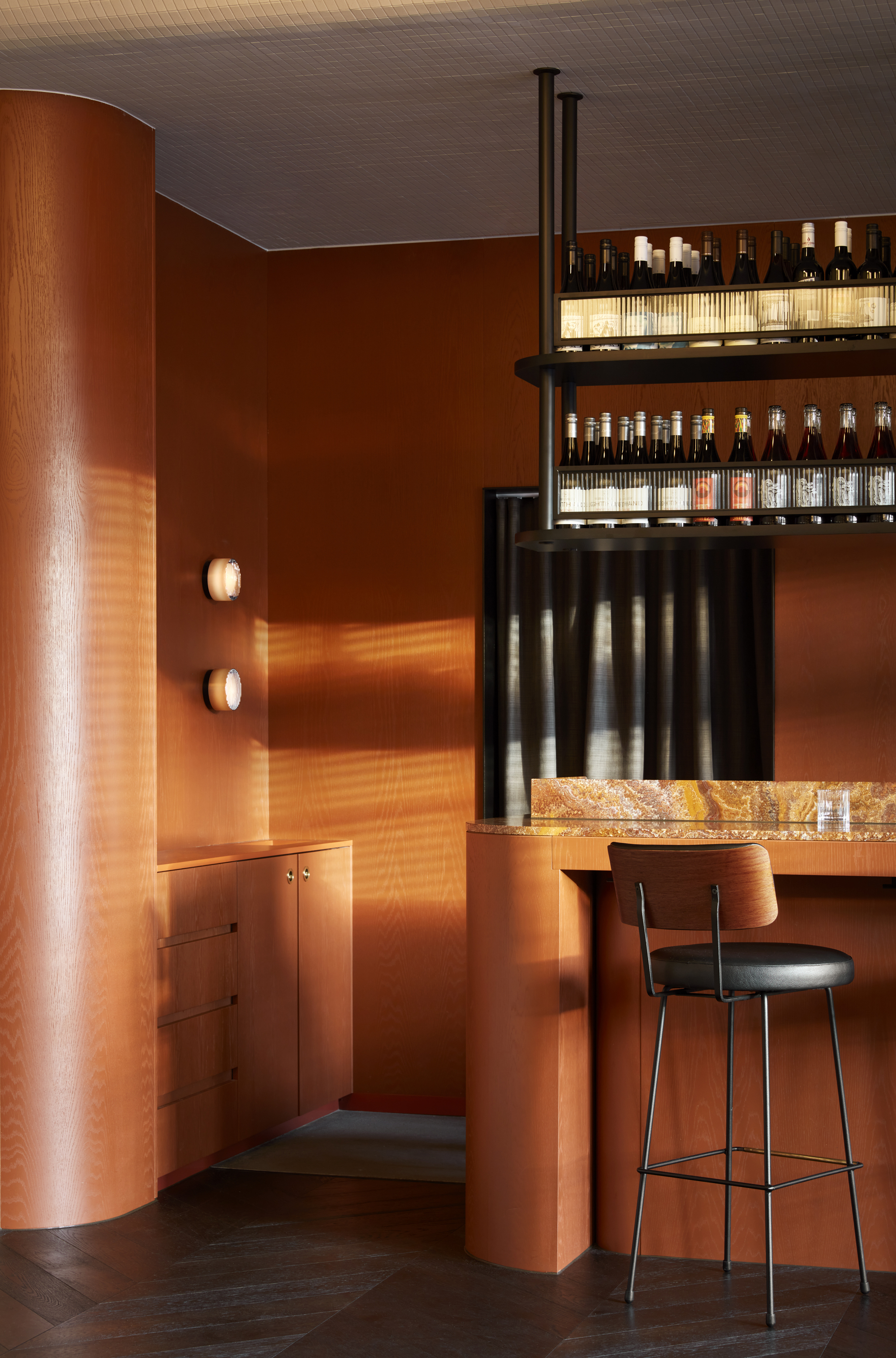 Curved copper-clad column beside bar counter with illuminated shelving and dark stovepipe vent