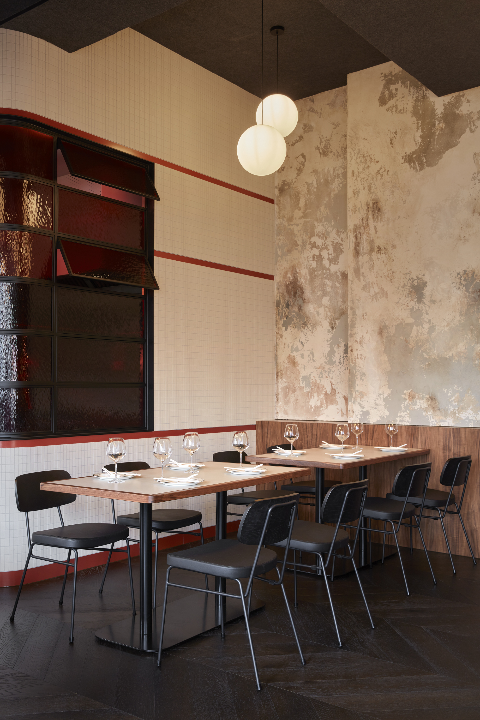 Dining tables against weathered plaster walls with dark wood shelving and white mosaic tile wainscoting