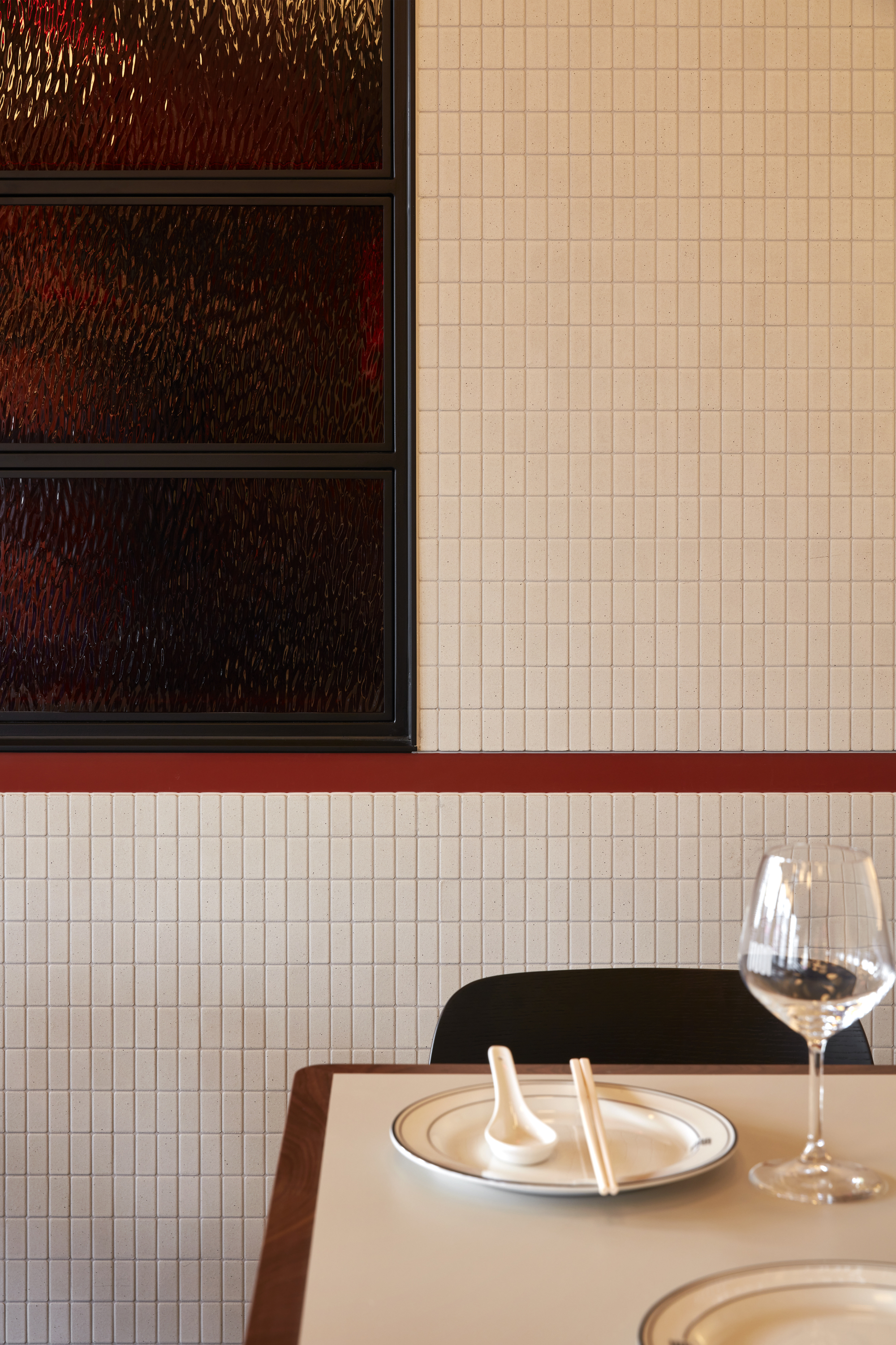 Detail of white mosaic tile wall with red trim meeting dark textured glass display shelves