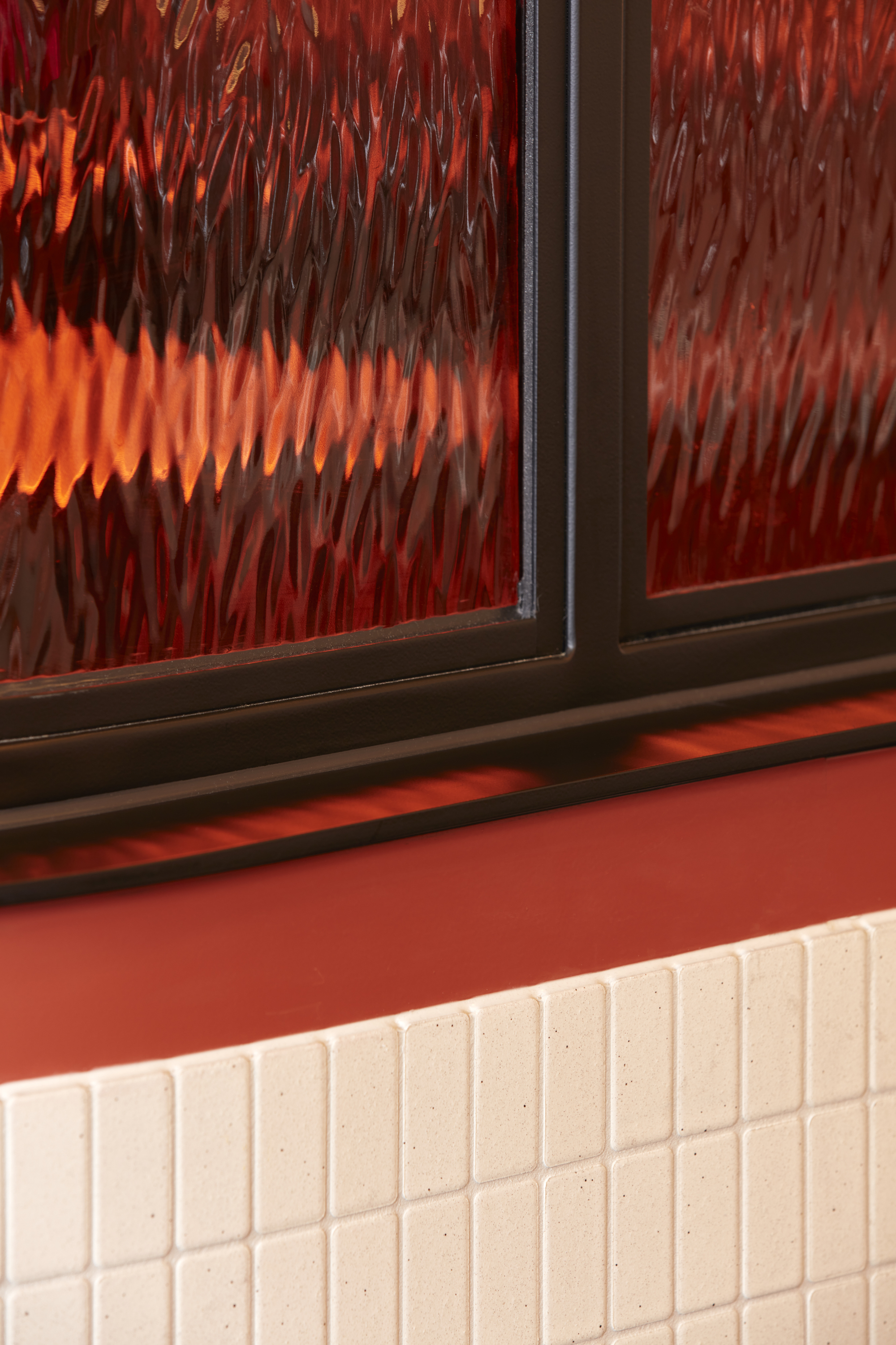 Textured glass window above white tile wainscoting with red wall and sill in warm interior light