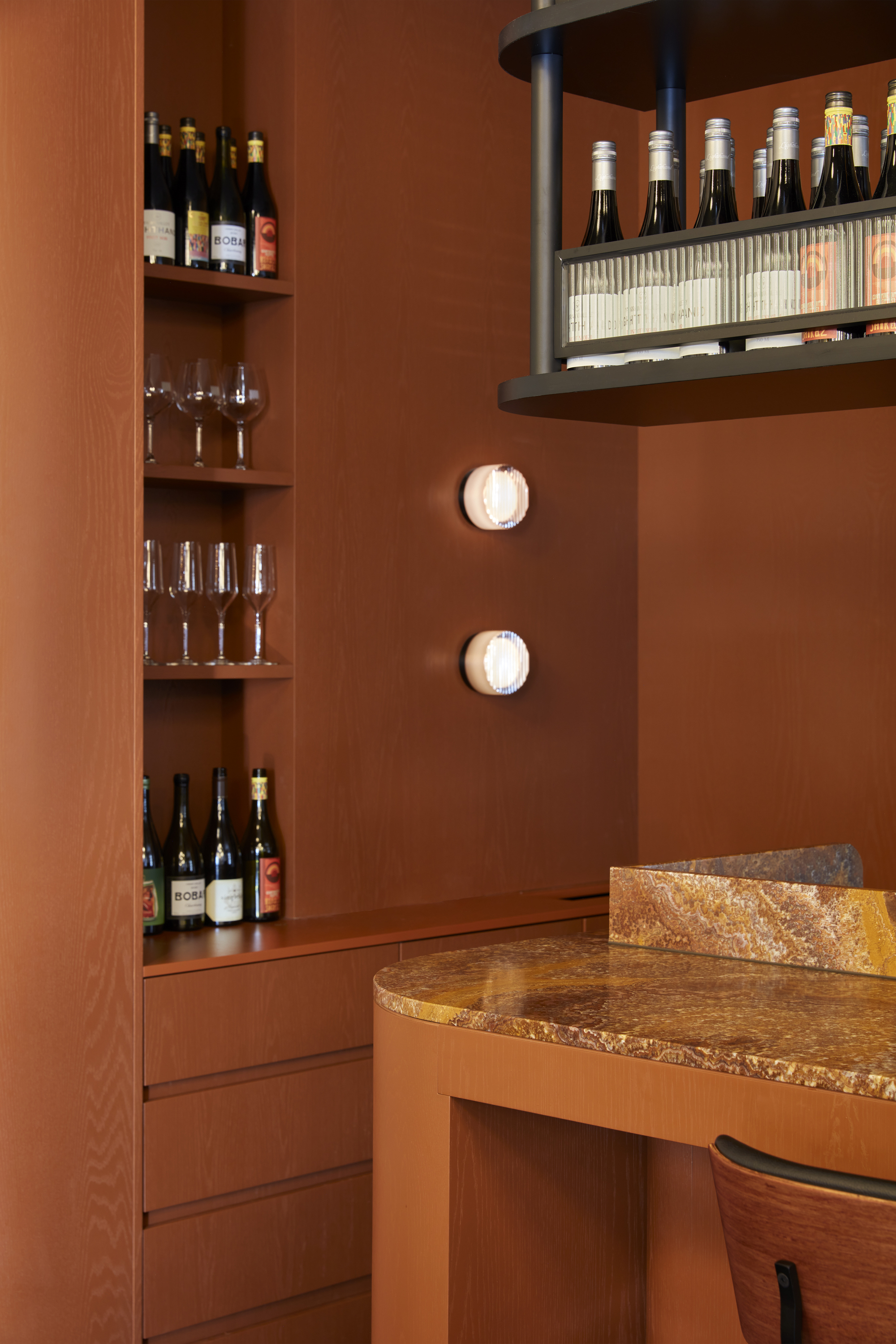 Bar area with timber shelving and suspended bottle rack above terrazzo-topped counter under wall sconces