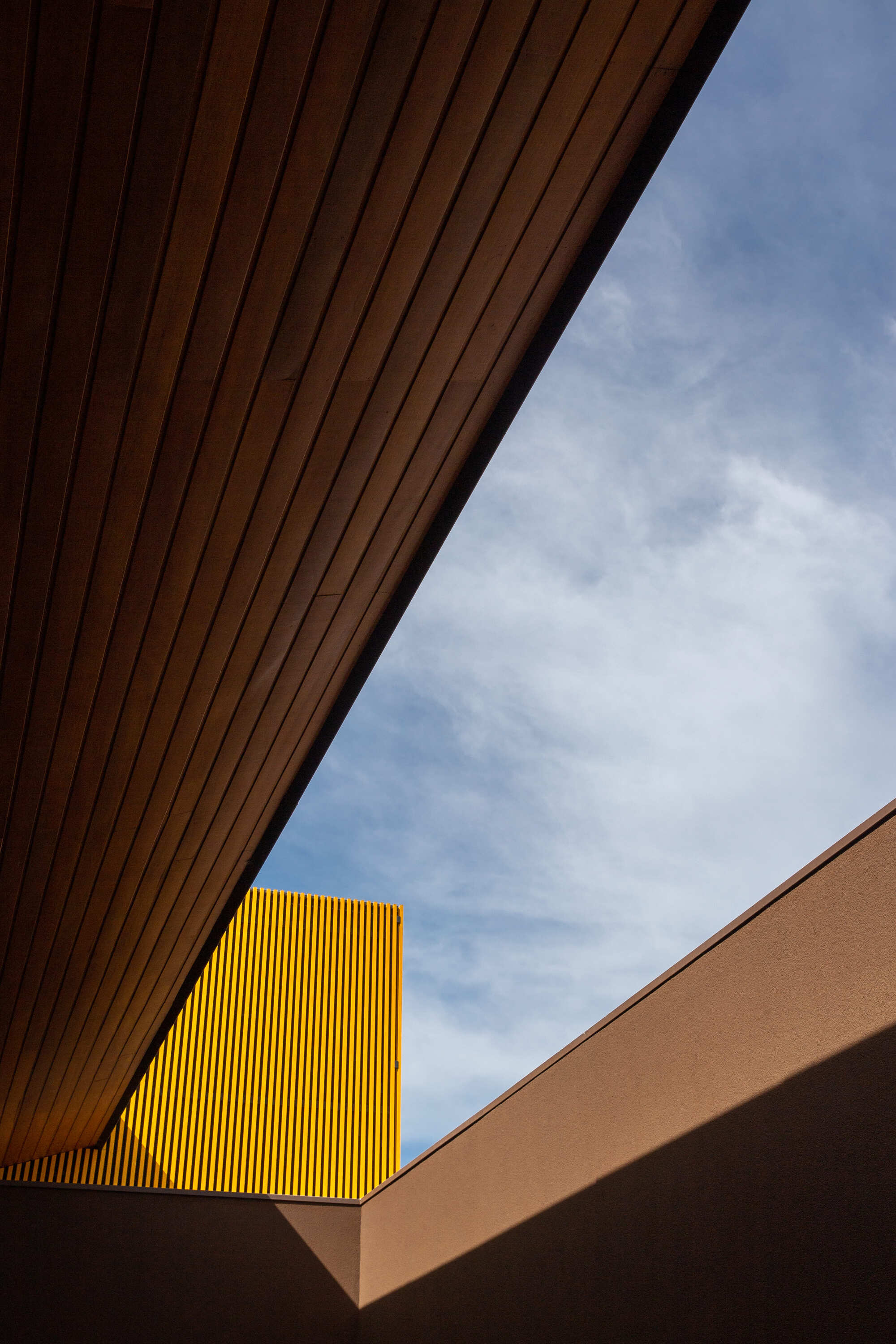 Looking up at the wood soffit framing the yellow perforated screen against blue sky