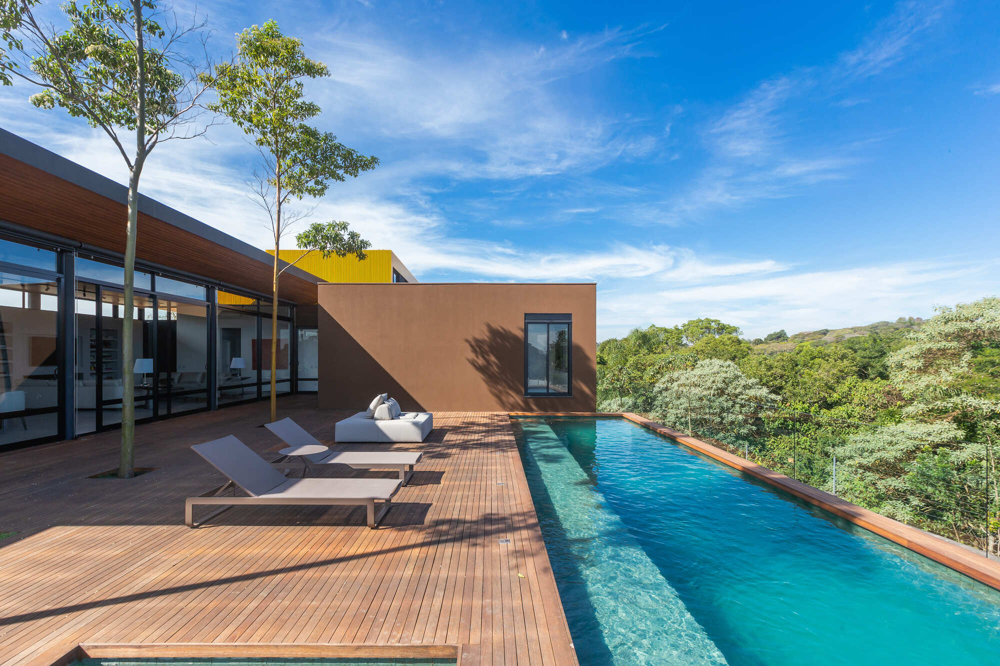 Pool deck with timber planking and glazed living pavilion overlooking hillside vegetation