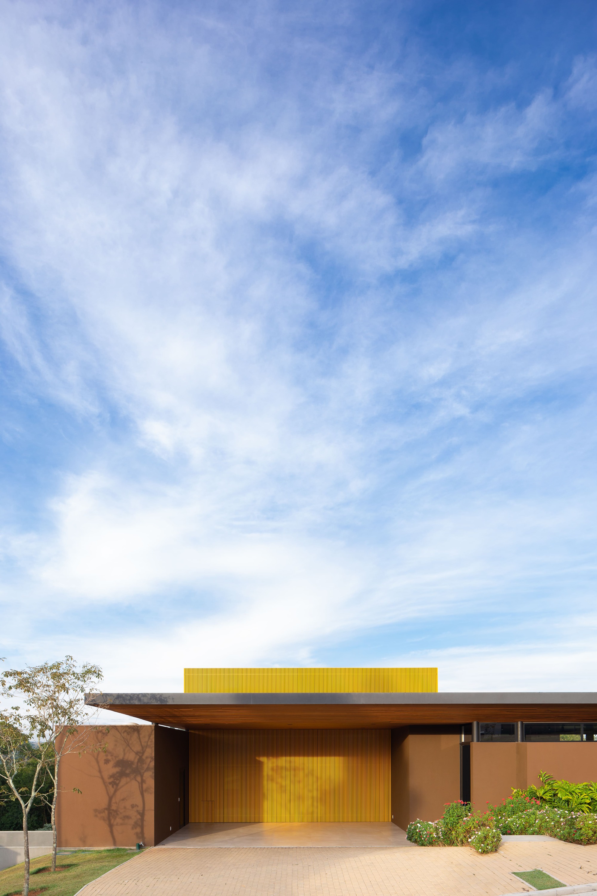 Entry facade with yellow portal and horizontal roof plane under wispy clouds