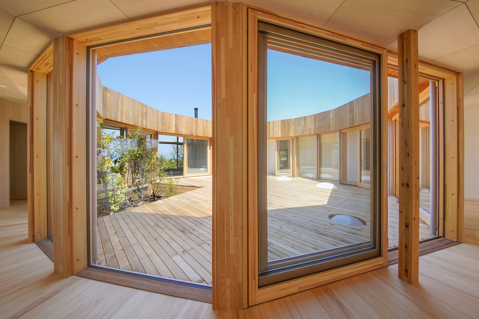Open timber-framed glass doors revealing a central courtyard deck framed by the curved building wings