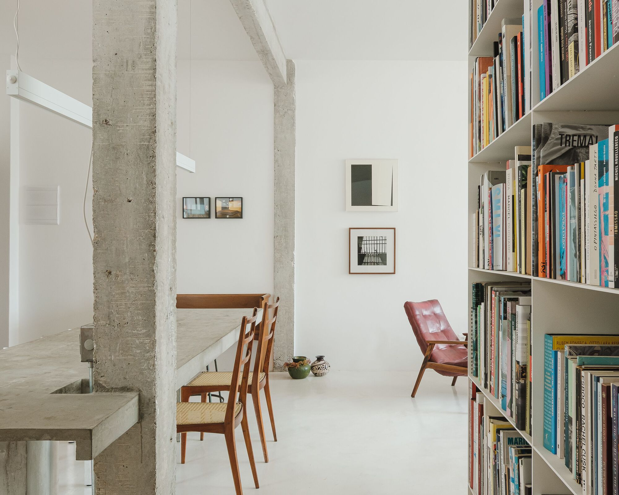 Double-height interior with exposed concrete columns, white walls, tall bookshelves and wooden dining chairs