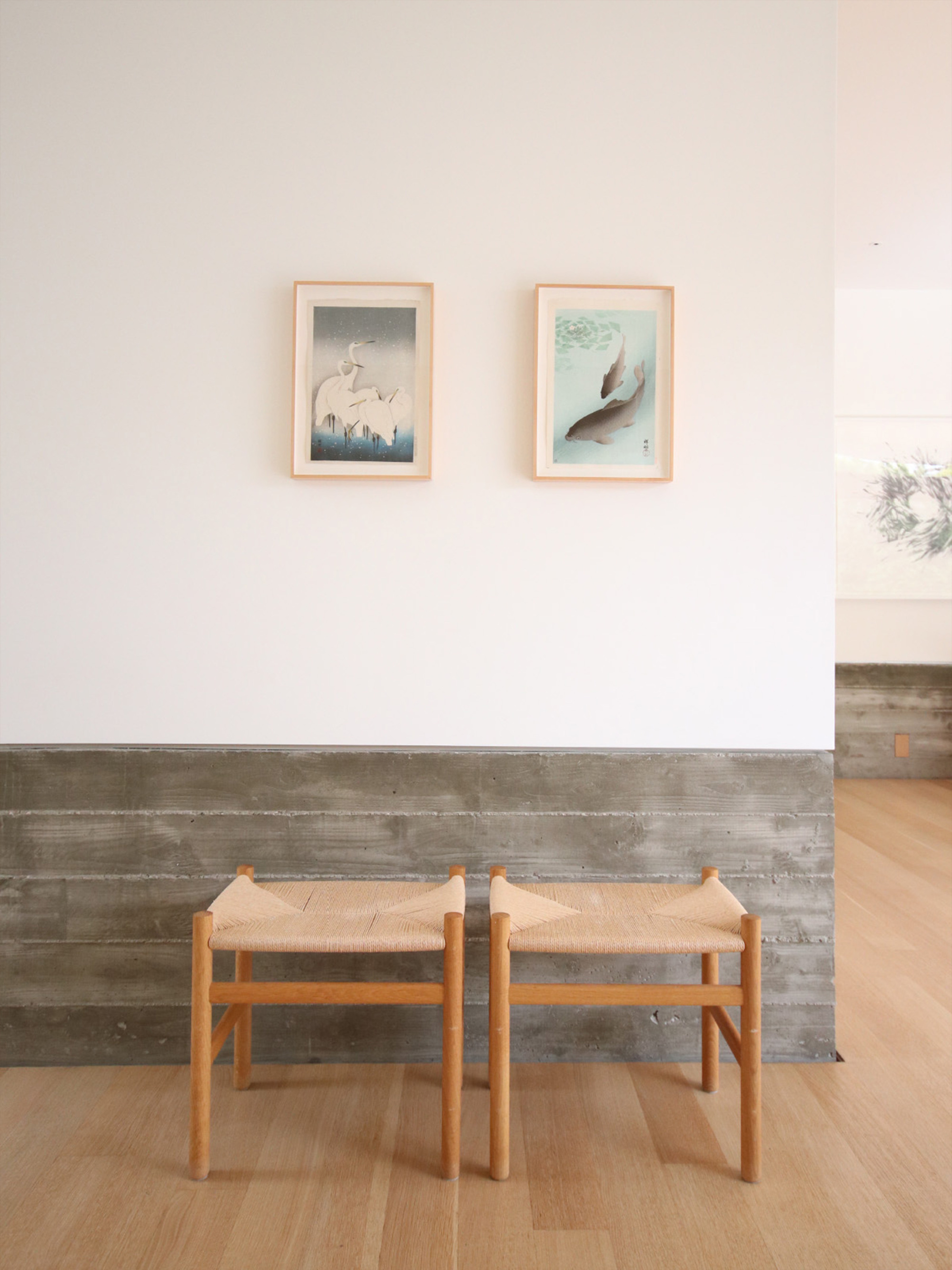 Two timber stools against a reclaimed wood wainscot below framed artworks on white wall