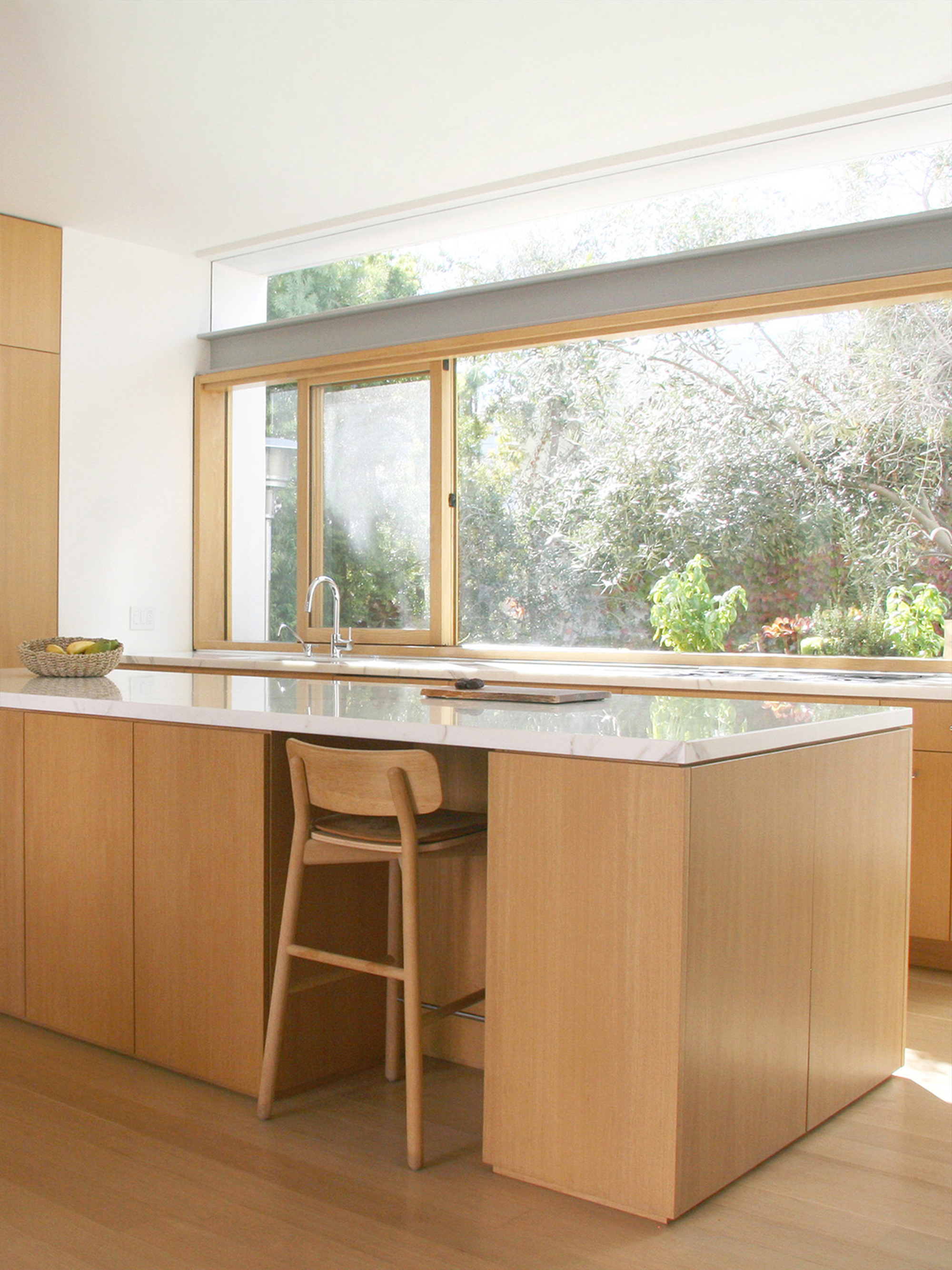 Kitchen island with white stone countertop facing timber-framed windows overlooking a garden
