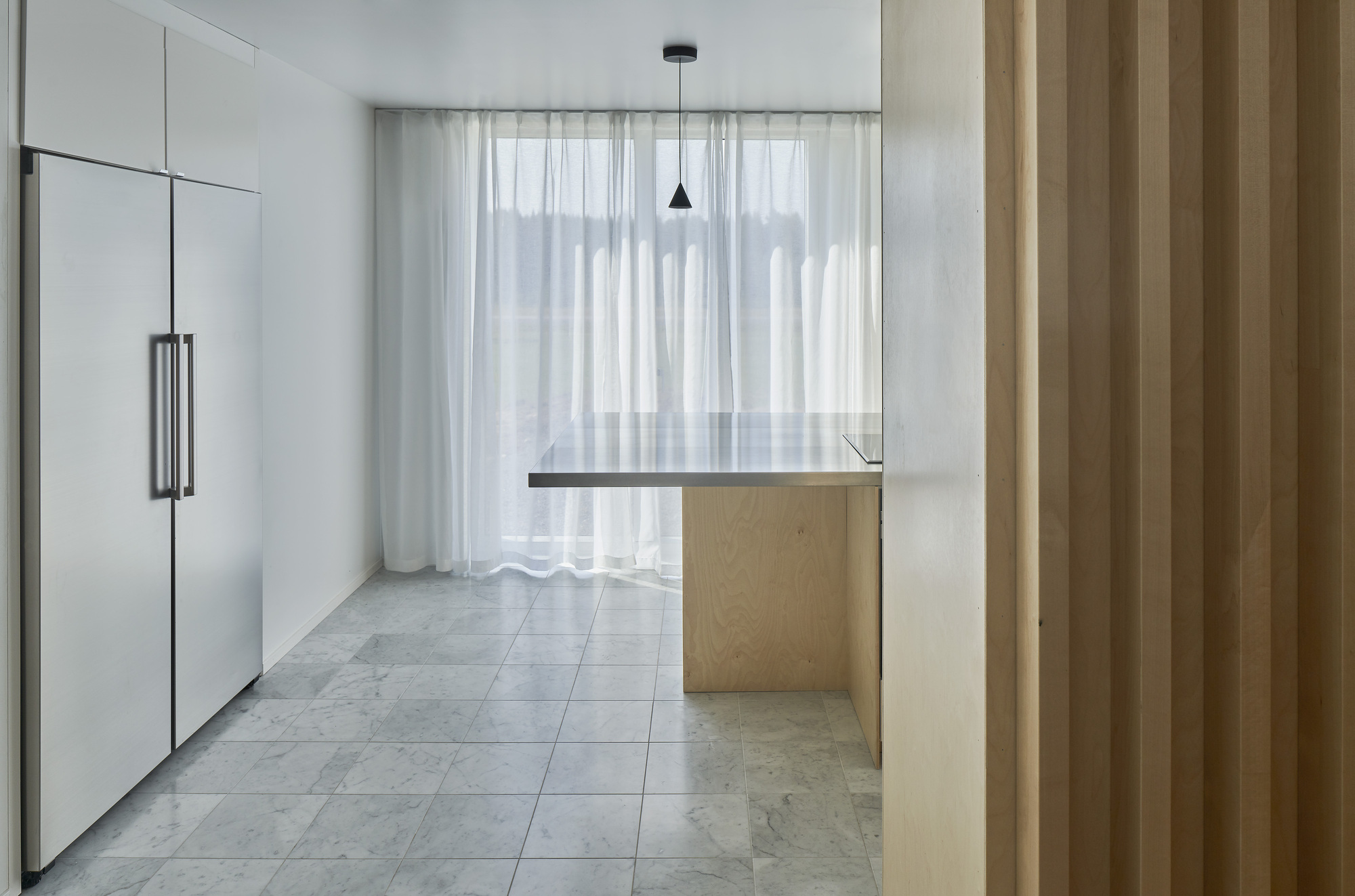 Kitchen with pale wood island and sheer curtains filtering light across grey tile floor