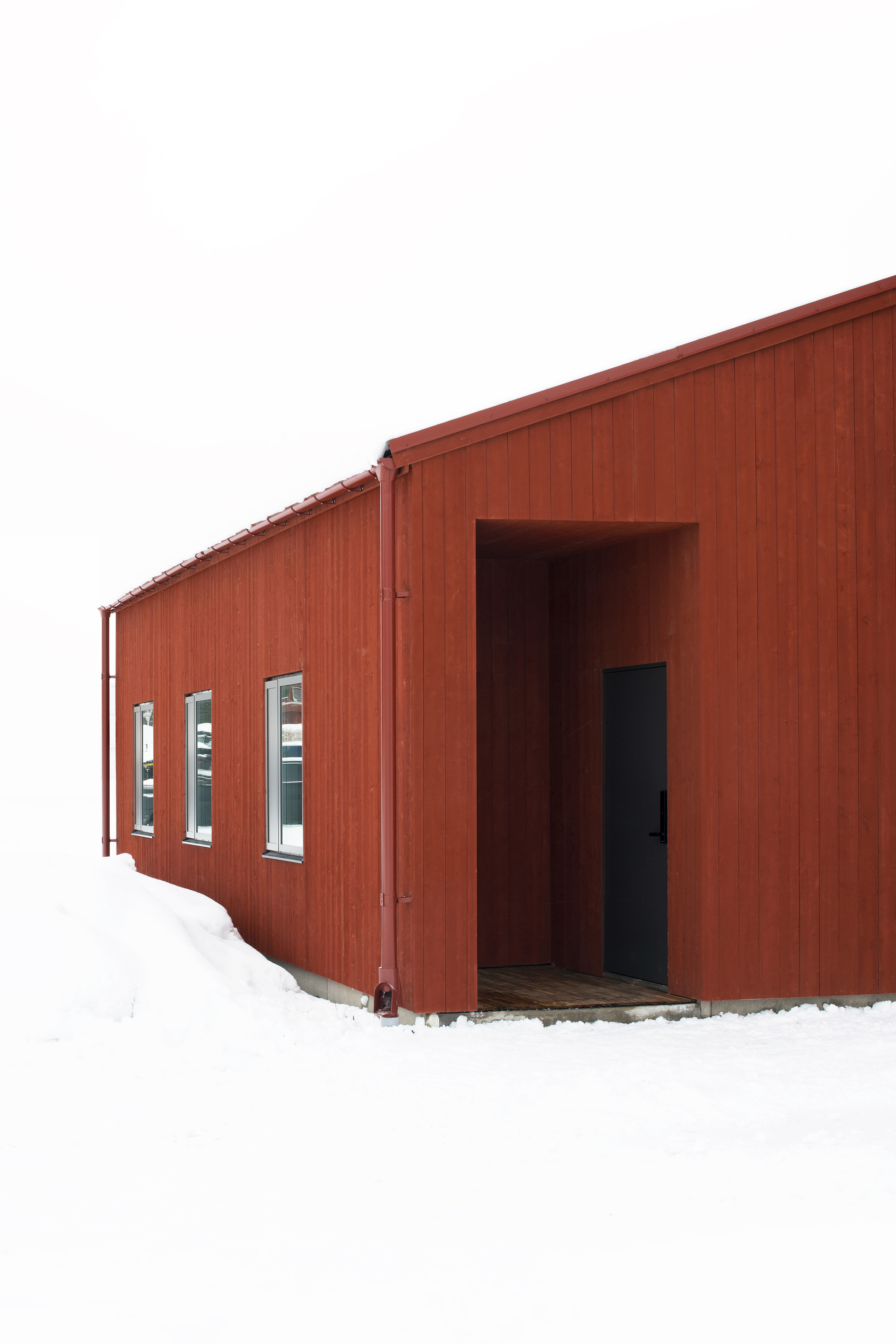 Recessed entrance in red wood cladding with a row of narrow windows in heavy winter snow