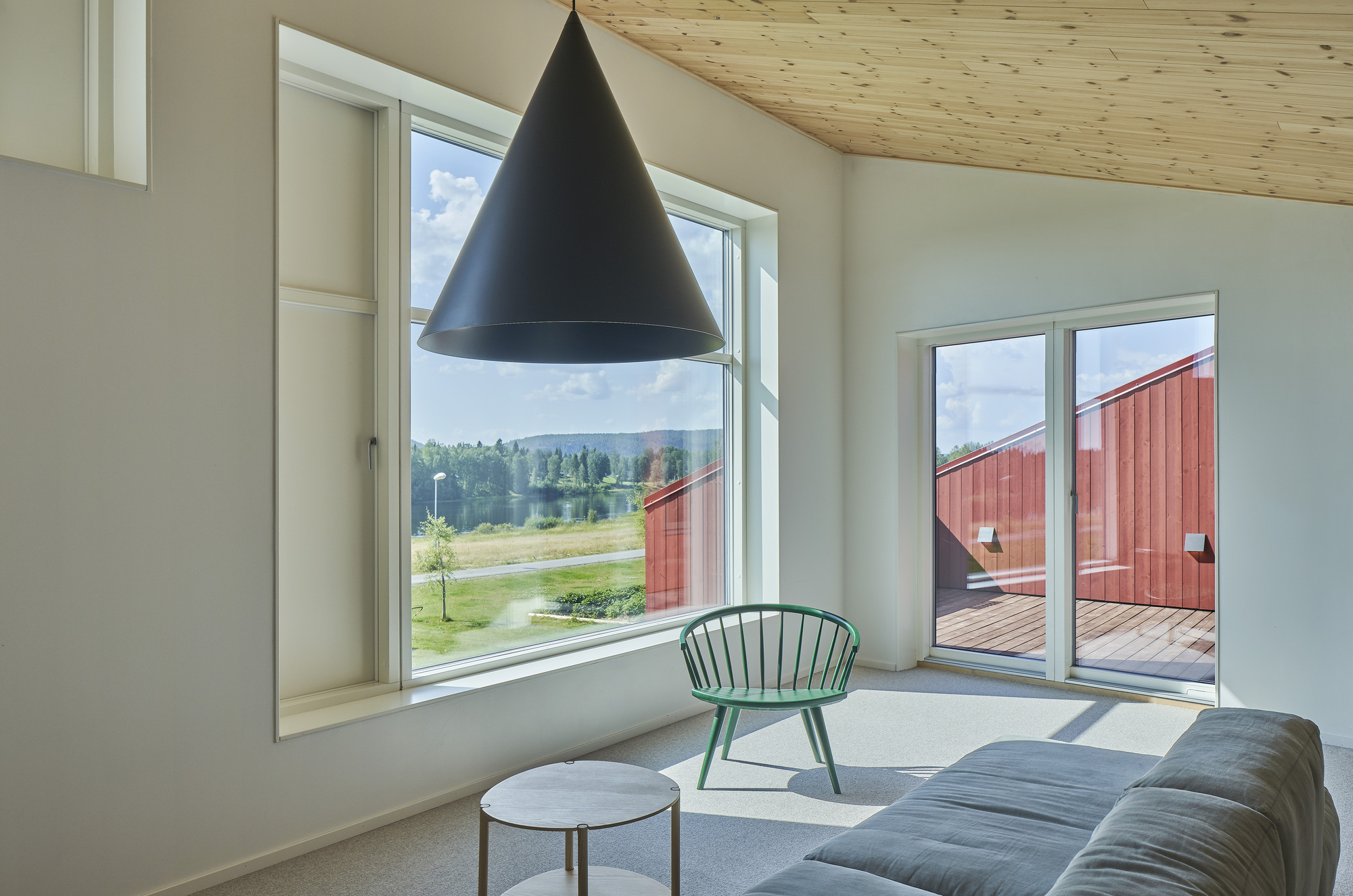 Living room with plywood ceiling and deep window reveals framing views of a red courtyard structure and landscape