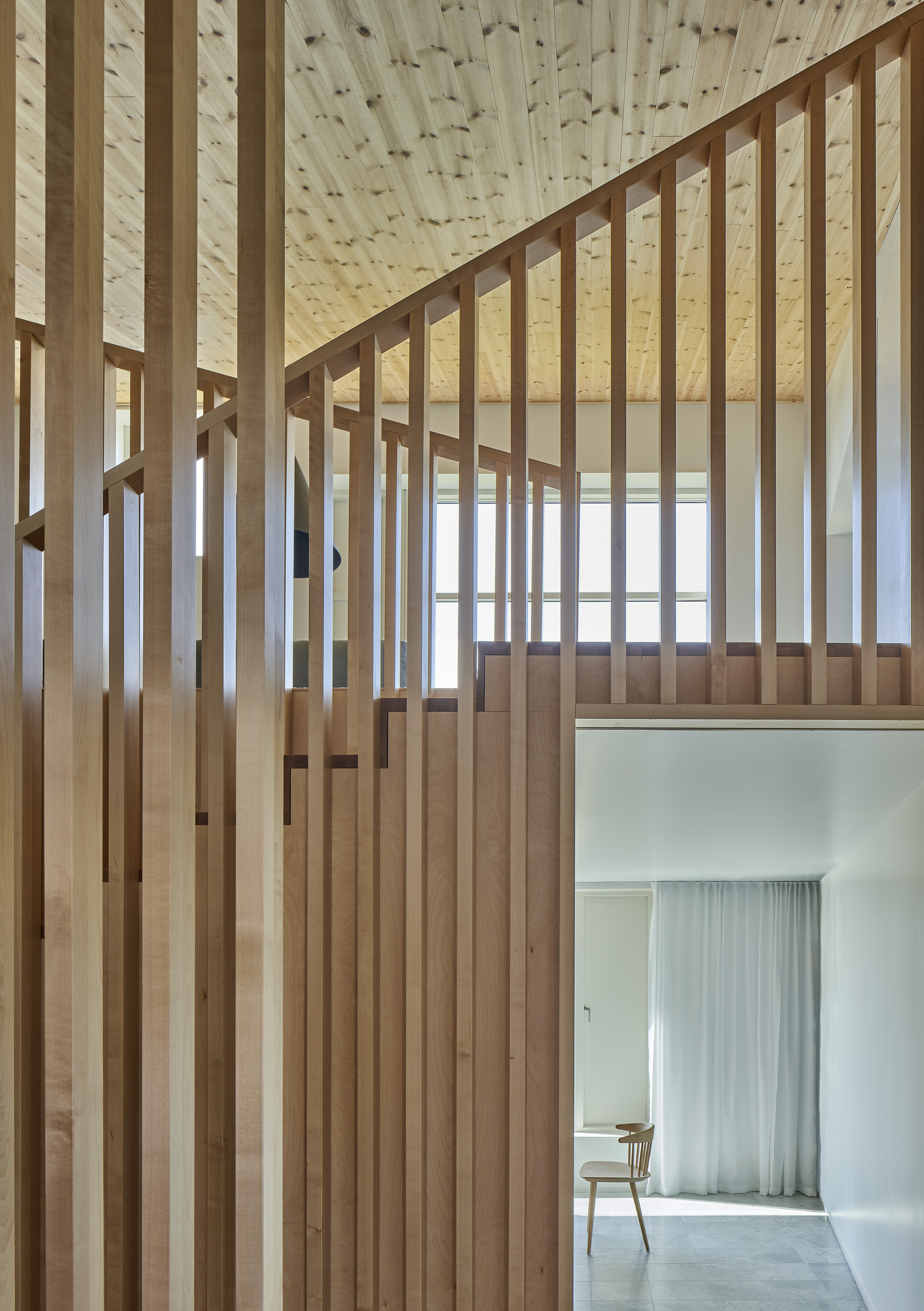 Double-height space with timber slat partitions framing an upper landing and doorway to a curtained room beyond