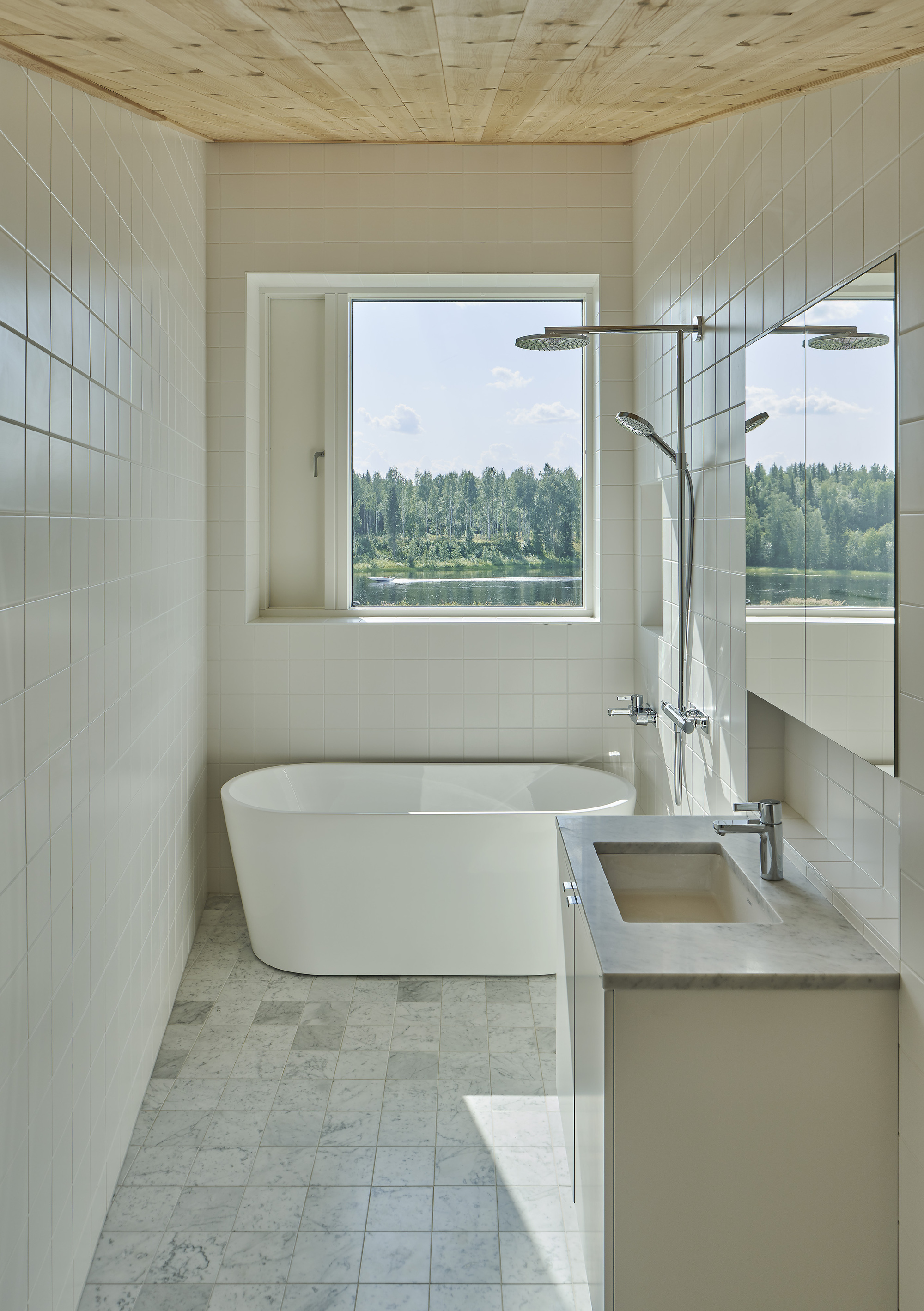Bathroom with freestanding tub and picture window framing views of forest and lake