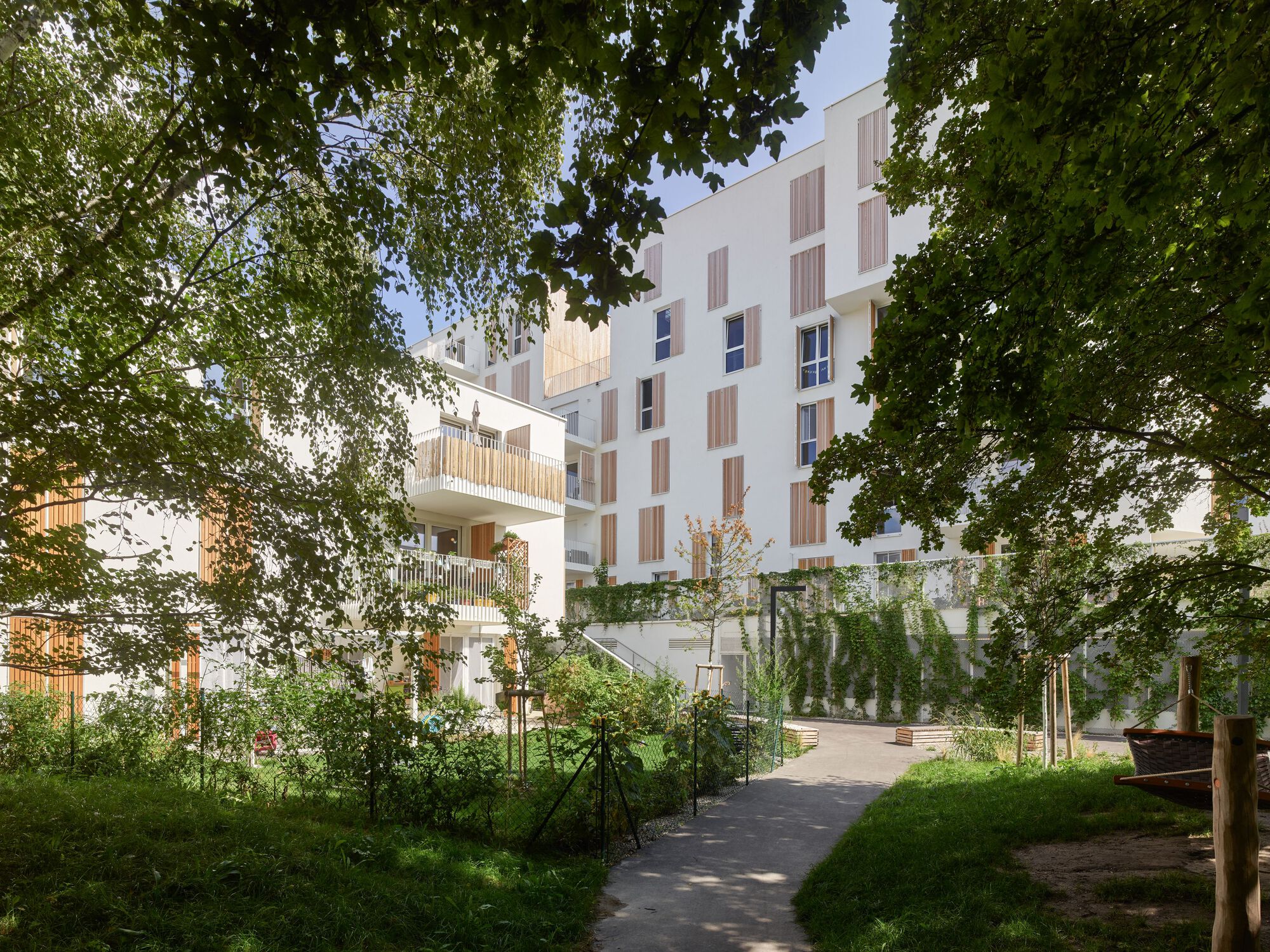 White residential blocks with timber shutters framed by mature trees and a garden pathway in summer