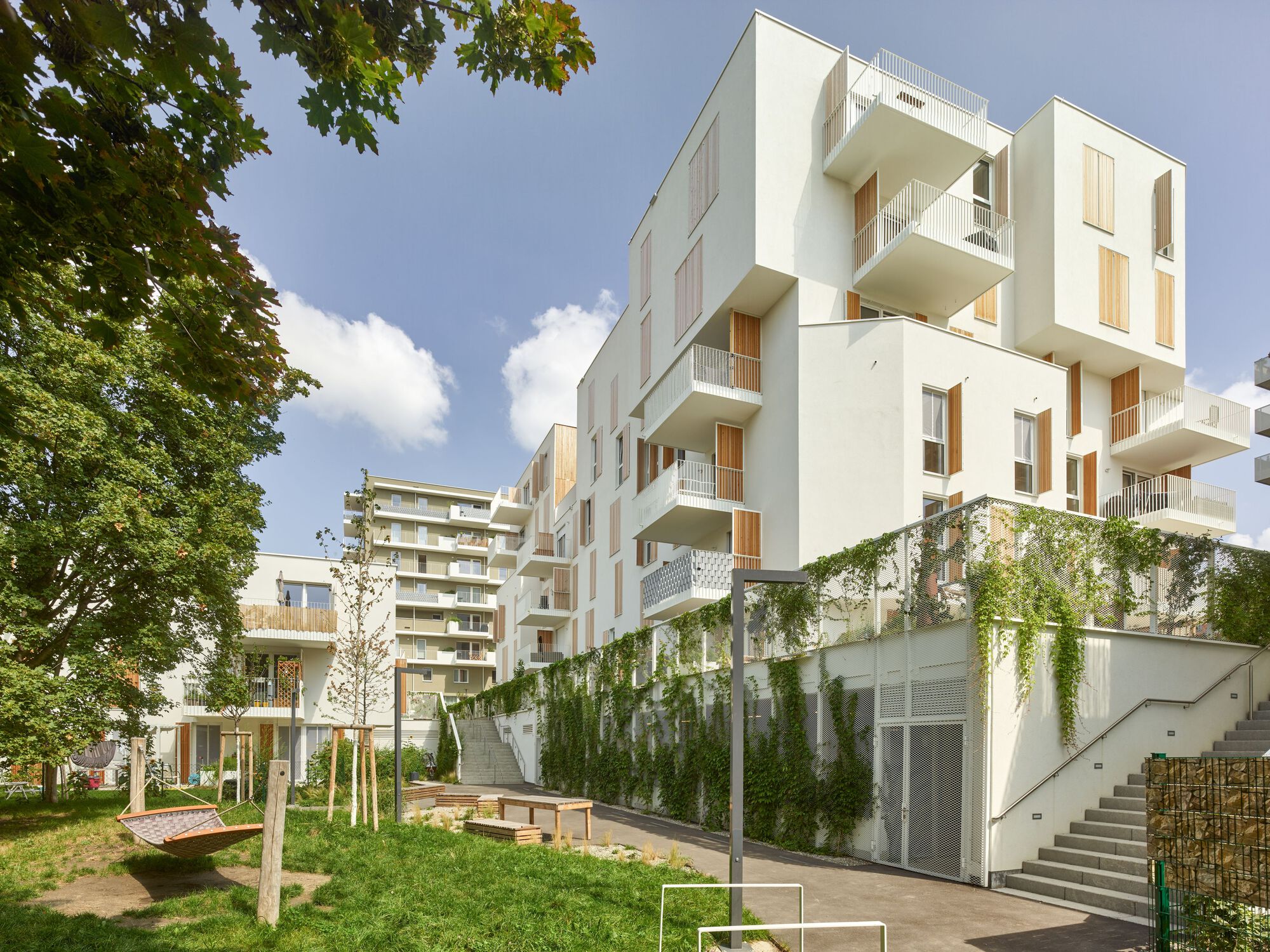 Courtyard view showing staggered white balconies and a green wall with climbing plants under blue sky