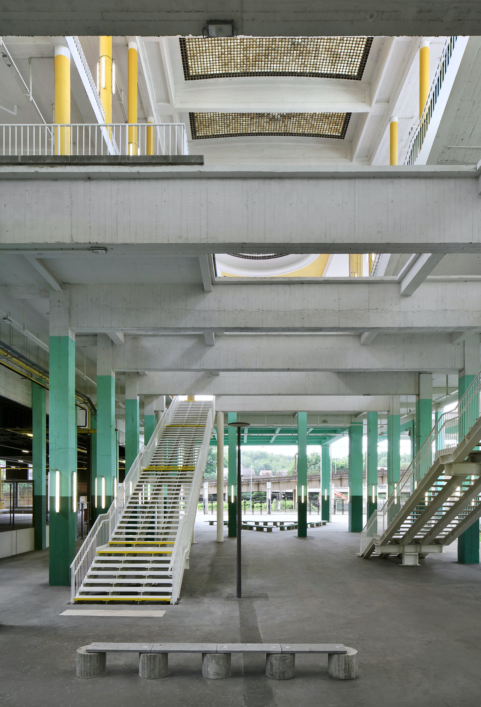 Ground floor interior with green columns, open steel stairs, and concrete bench beneath exposed structural beams