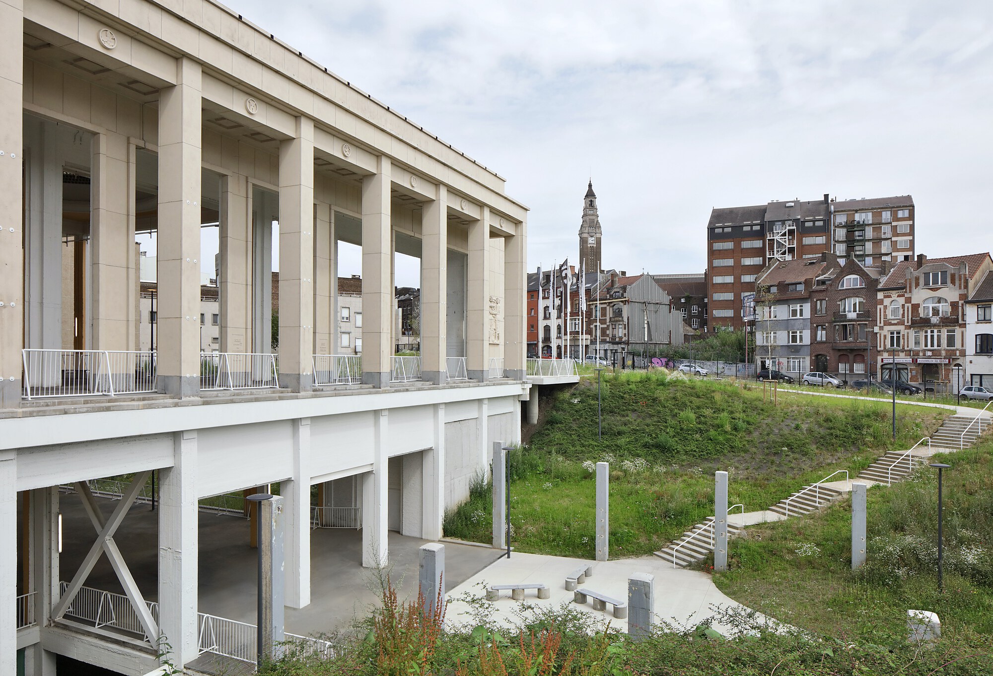 Elevated colonnade with precast columns overlooking a grassed embankment and surrounding urban buildings