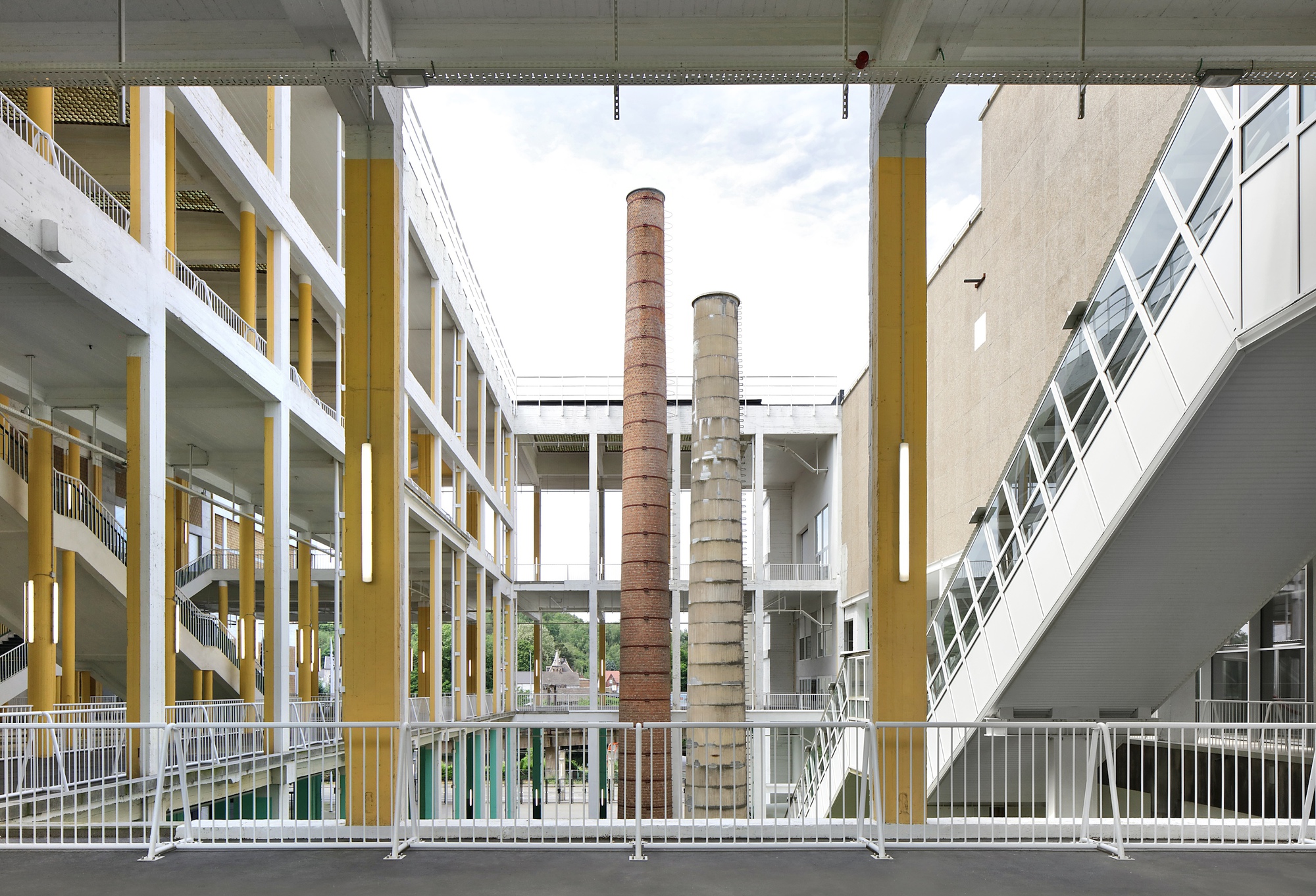 Central courtyard view framed by yellow structural columns with two preserved industrial brick chimneys