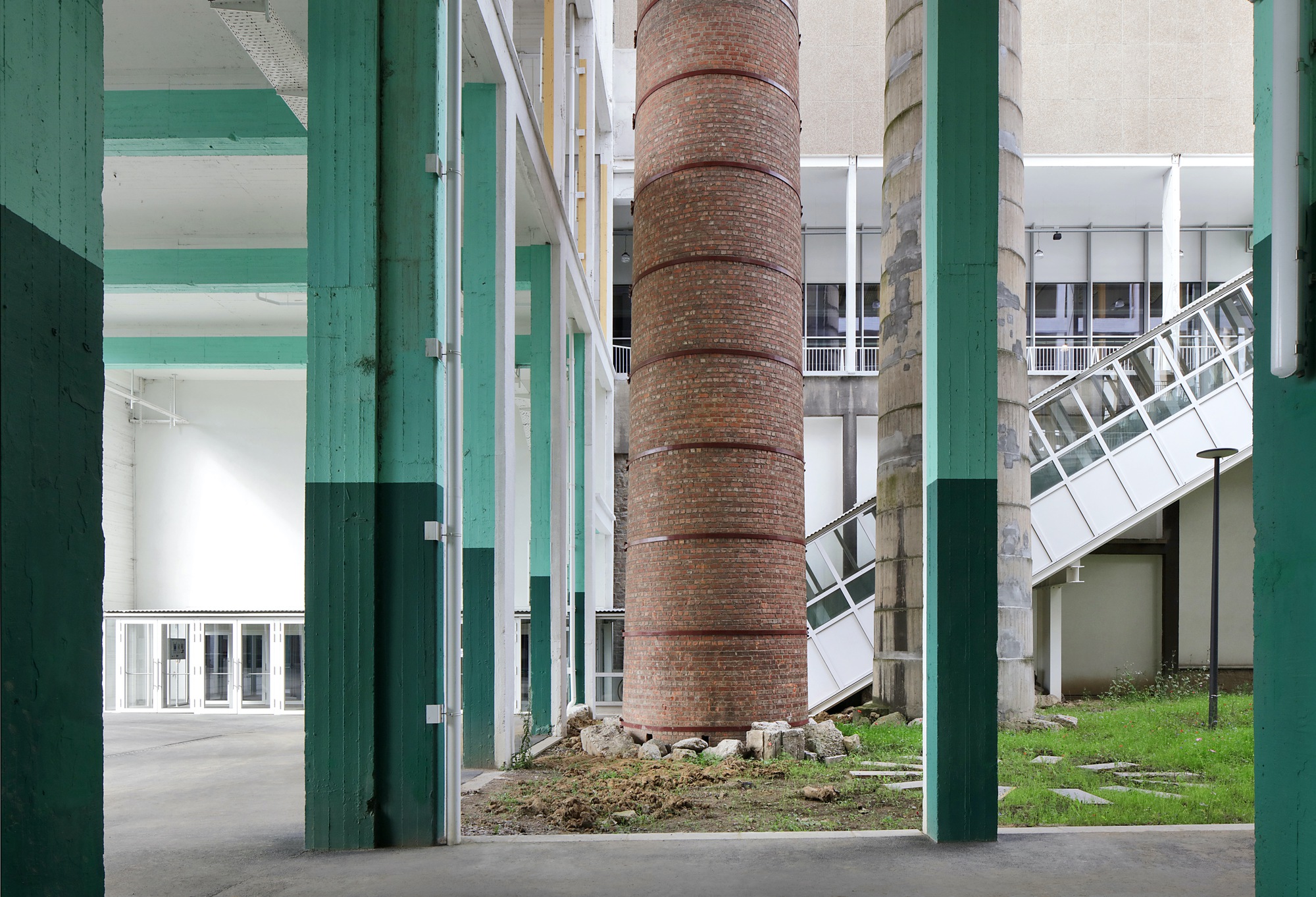 View through green-painted columns toward a preserved brick chimney and planted courtyard area