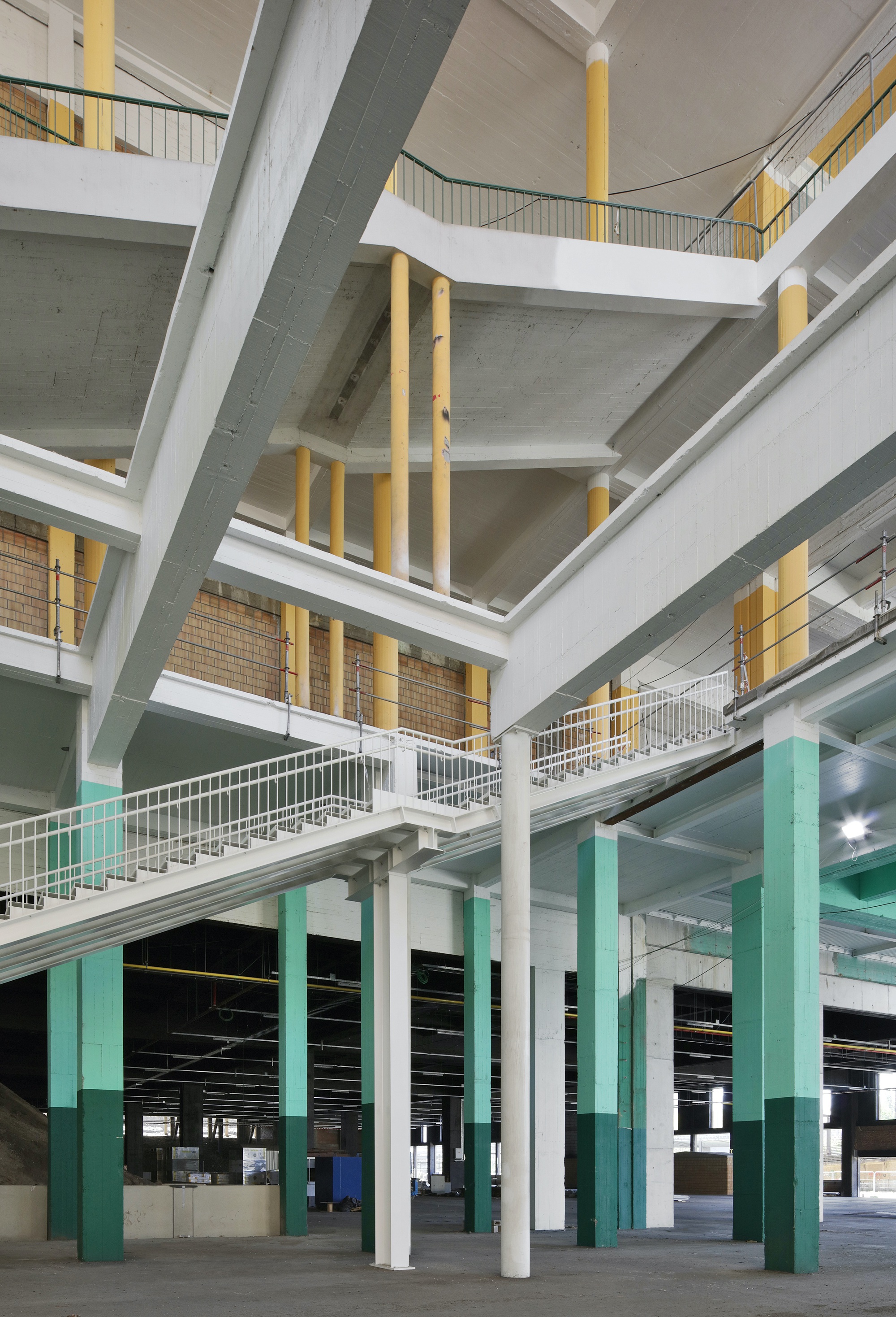 Multi-level atrium with white and turquoise columns supporting concrete slabs and interconnected walkways