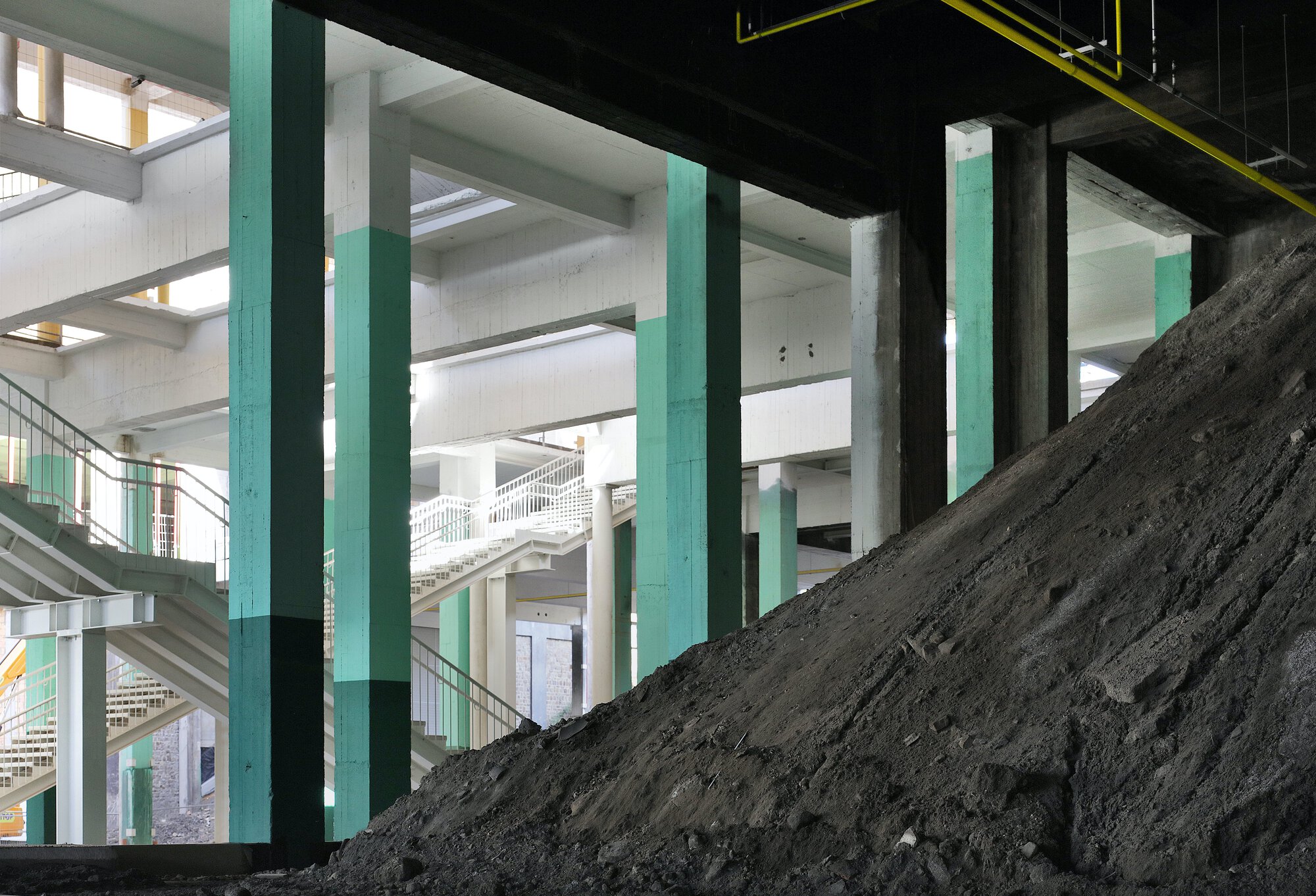 Interior view with turquoise columns and a dark earthen slope rising through the floor