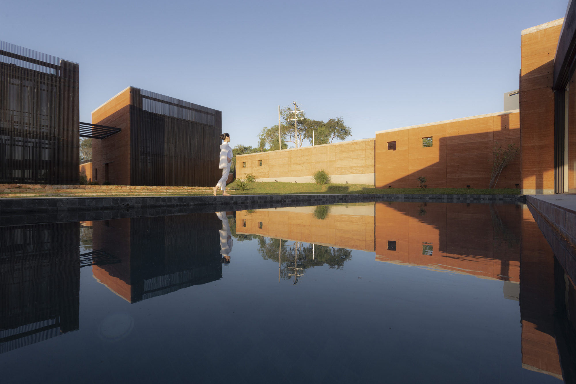Reflecting pool mirroring the corrugated metal and rammed earth facades with a figure walking