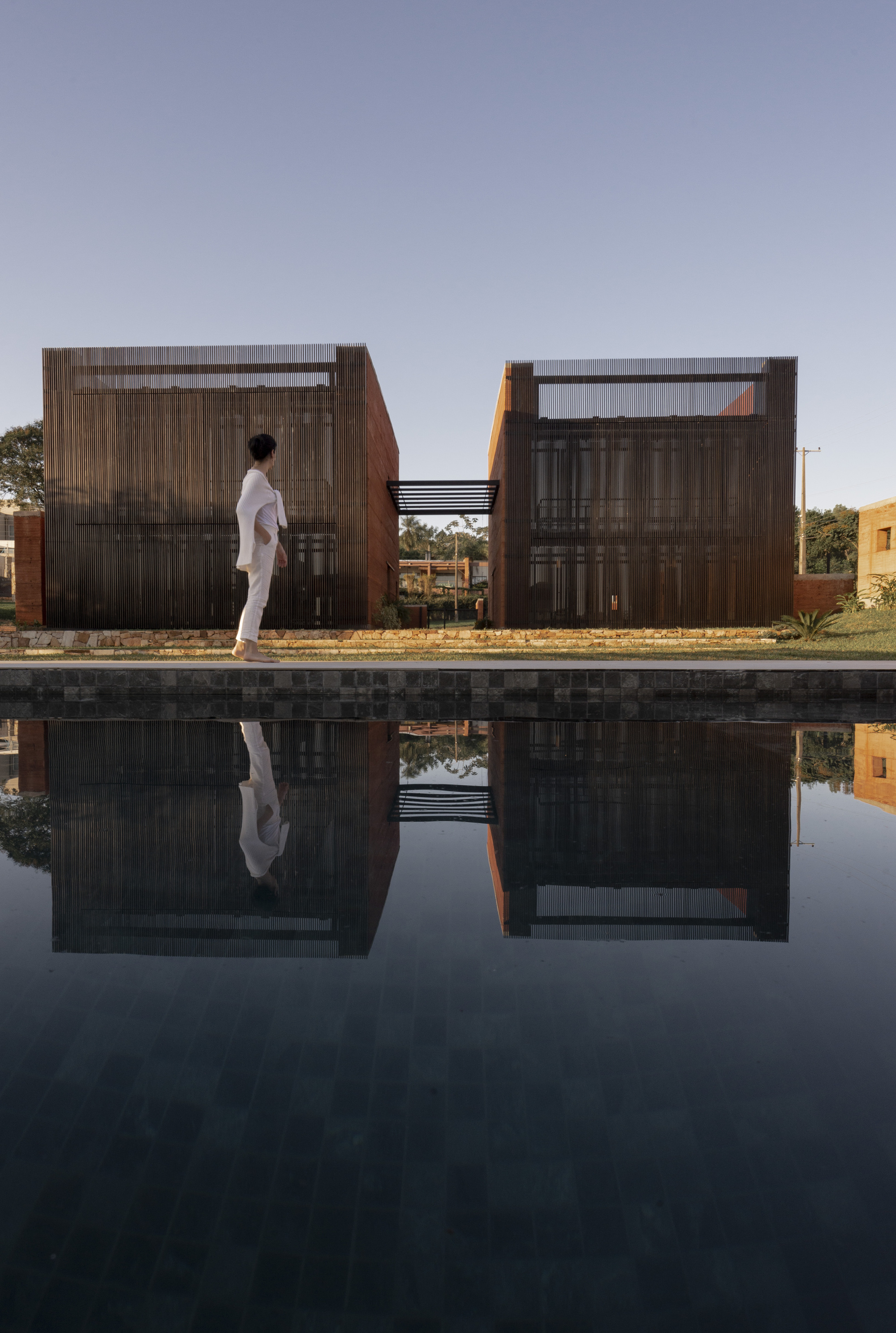 Figure walking beside reflecting pool with corrugated metal screen facades at dusk