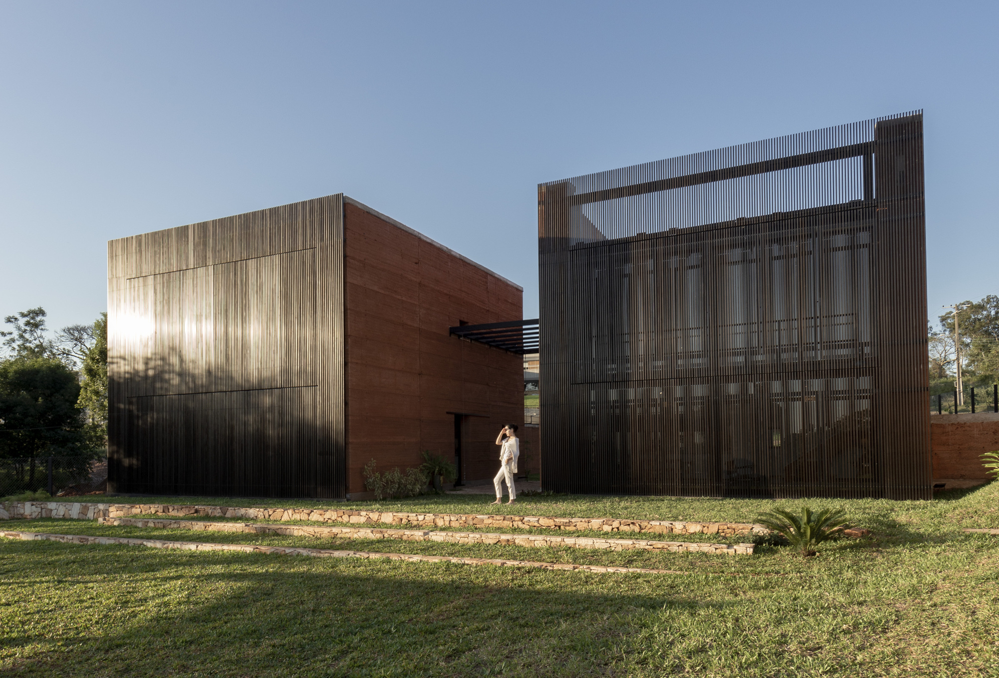 Frontal view of corrugated metal screen and rammed earth volumes in low afternoon sun