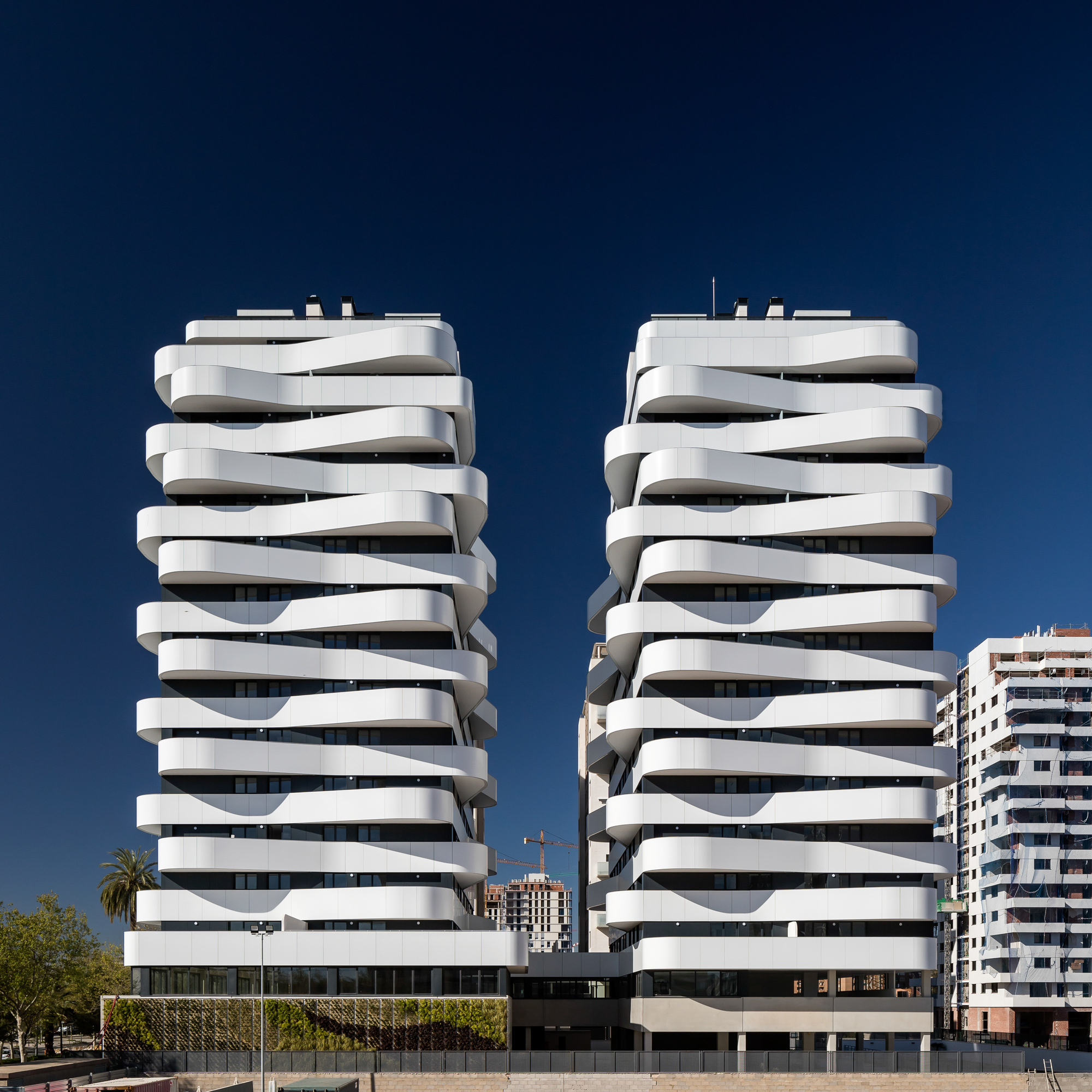 Twin residential towers with stacked ribbon balconies under a deep blue sky