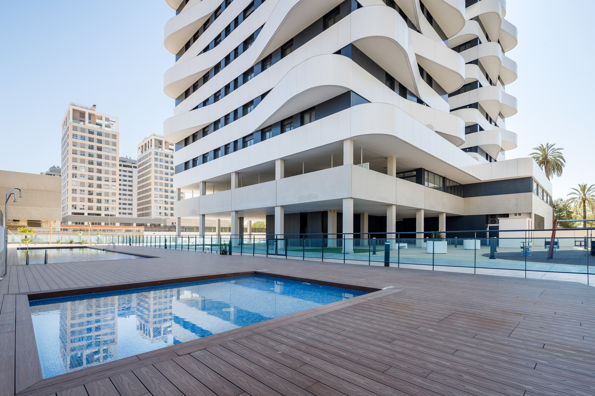 Ground-level pool deck with timber decking and glass railing below the curved balconies