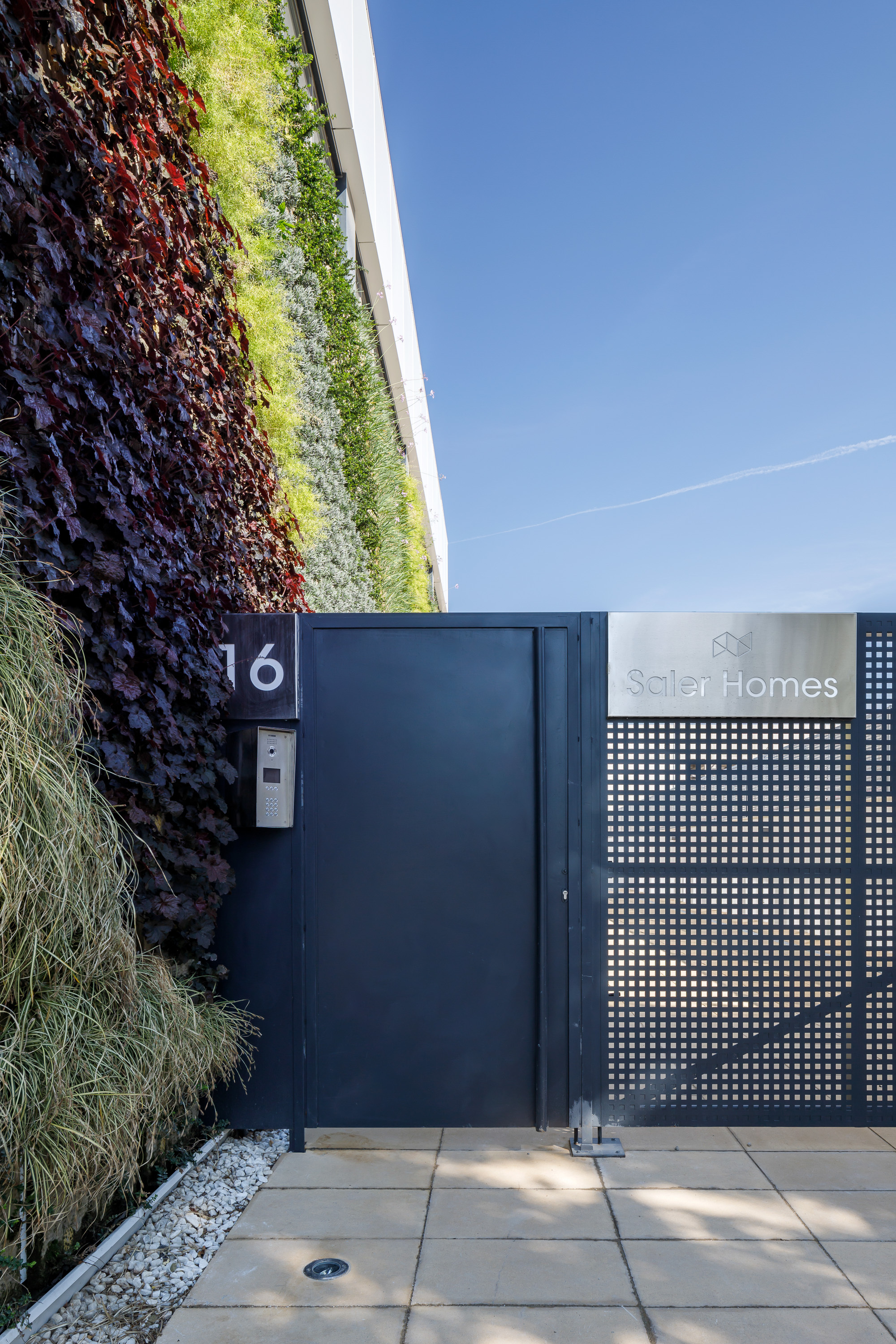 Entry gate with perforated metal panel and vertical planted wall of purple and green foliage