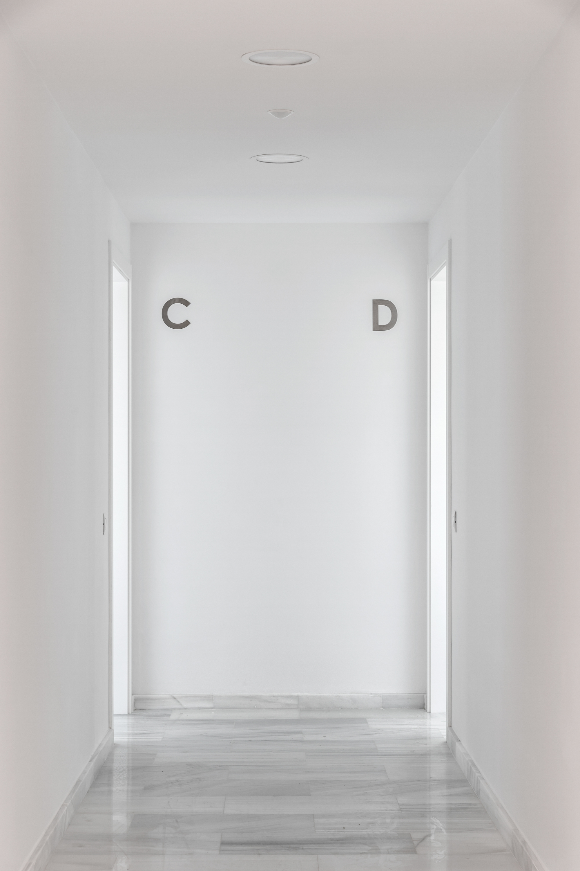 White corridor with pale timber flooring leading to a backlit wall marked with letters C and D