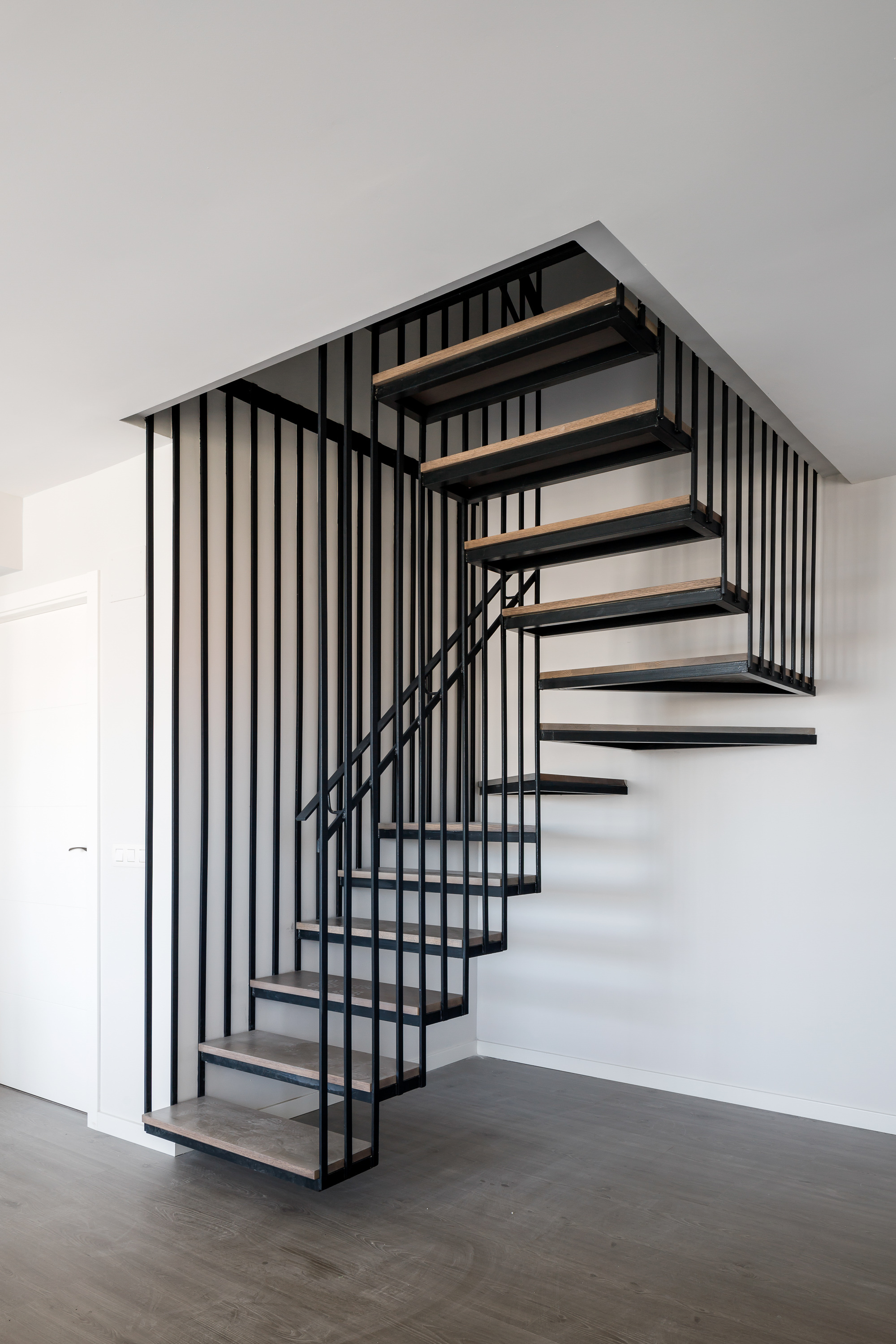 Black steel and timber staircase with vertical rod balustrade ascending through a white interior
