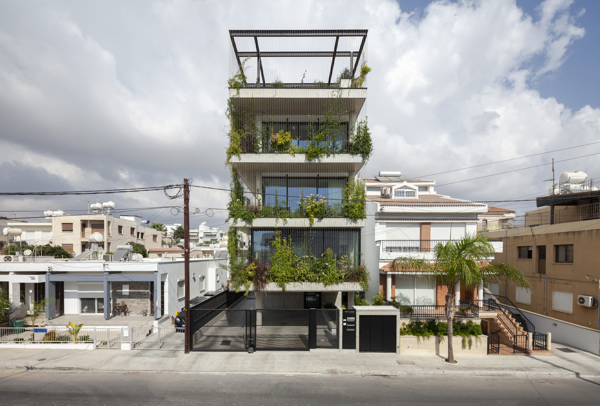 Front elevation showing stacked planted terraces between vertical louvers and neighboring residential buildings