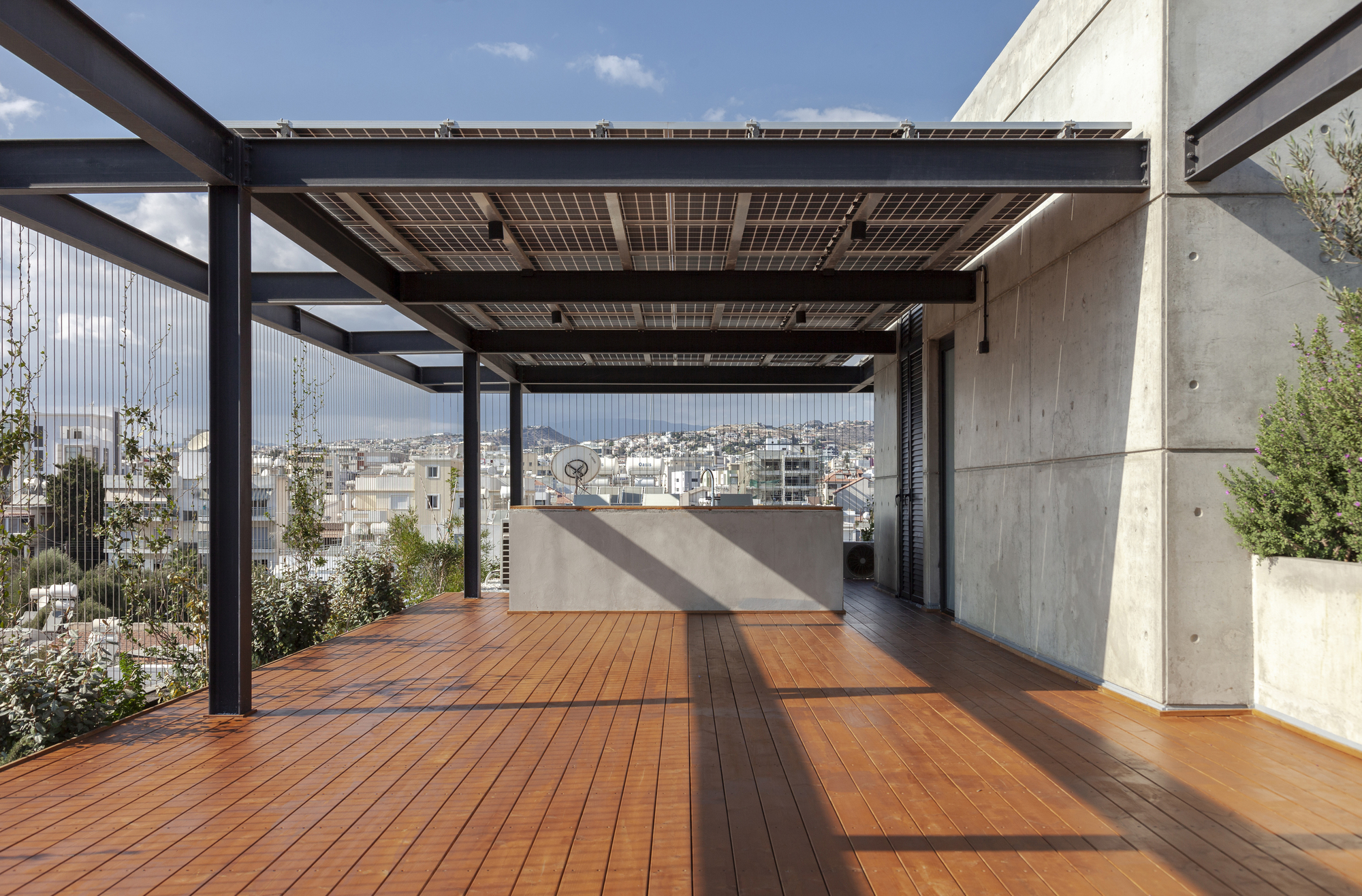 Rooftop terrace with solar panel canopy on steel beams above timber decking and concrete walls