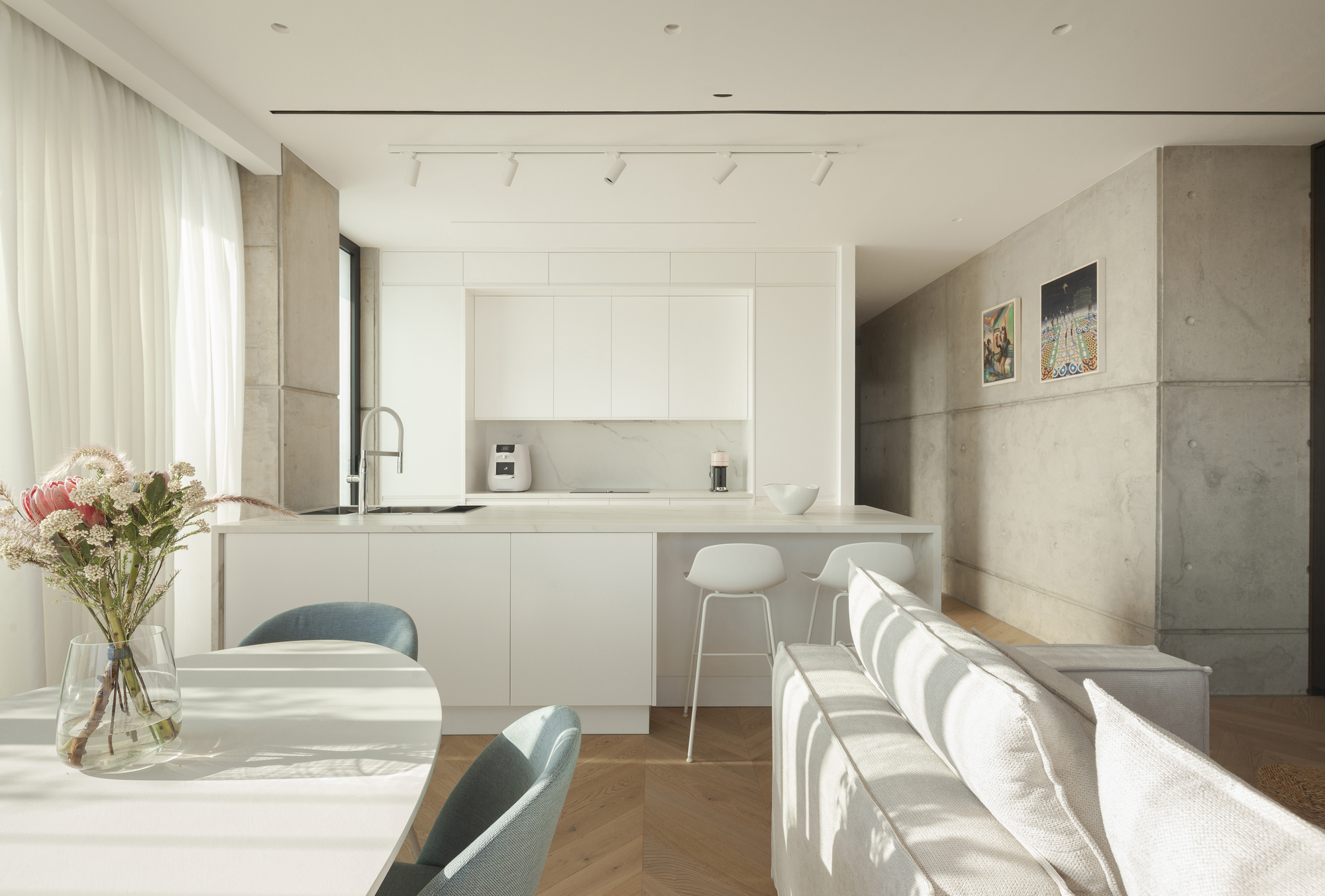 Open-plan kitchen and dining area with white cabinetry and concrete wall panels under soft daylight