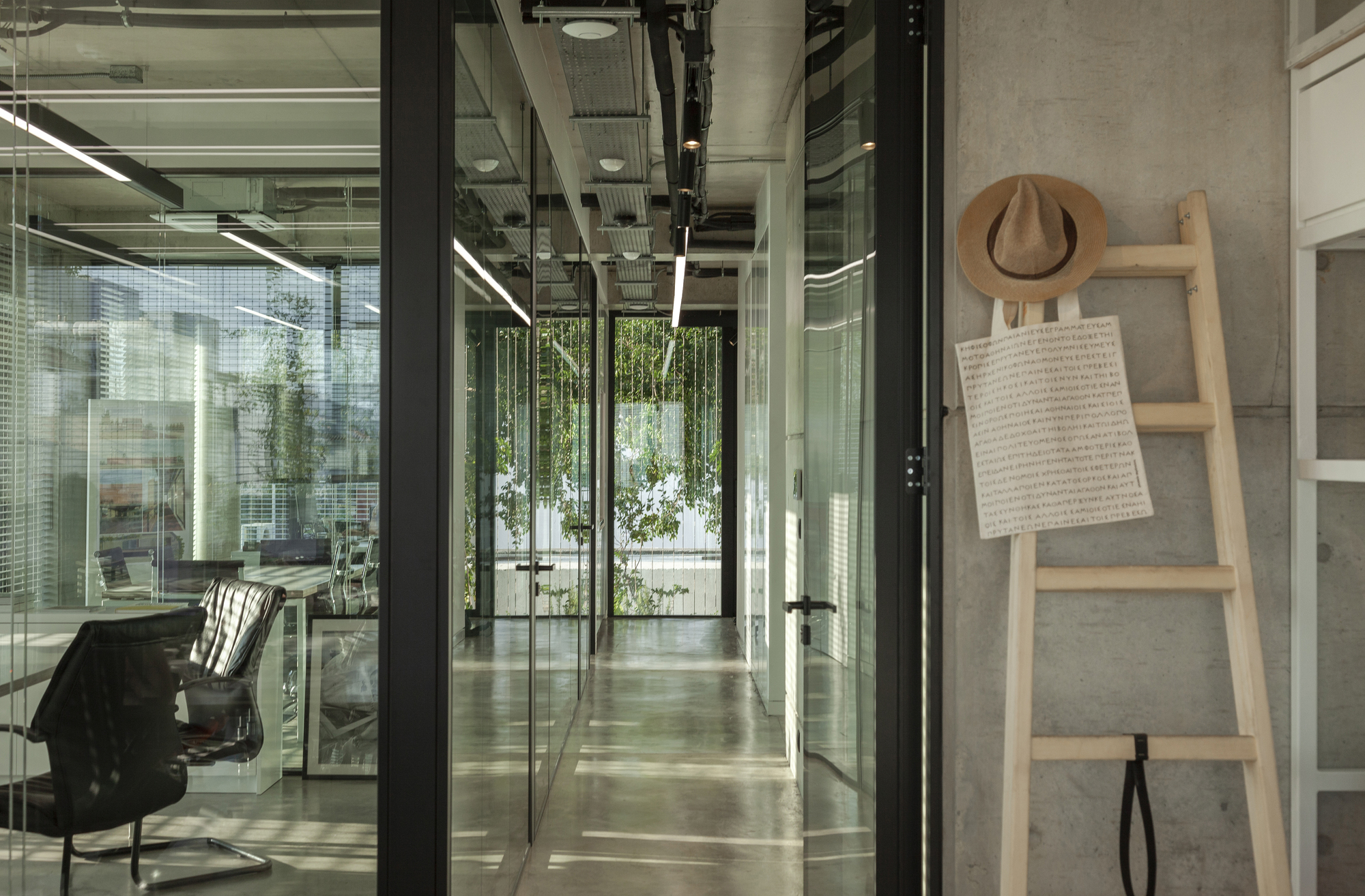 Glass corridor with black steel frames looking toward an interior courtyard with hanging plants