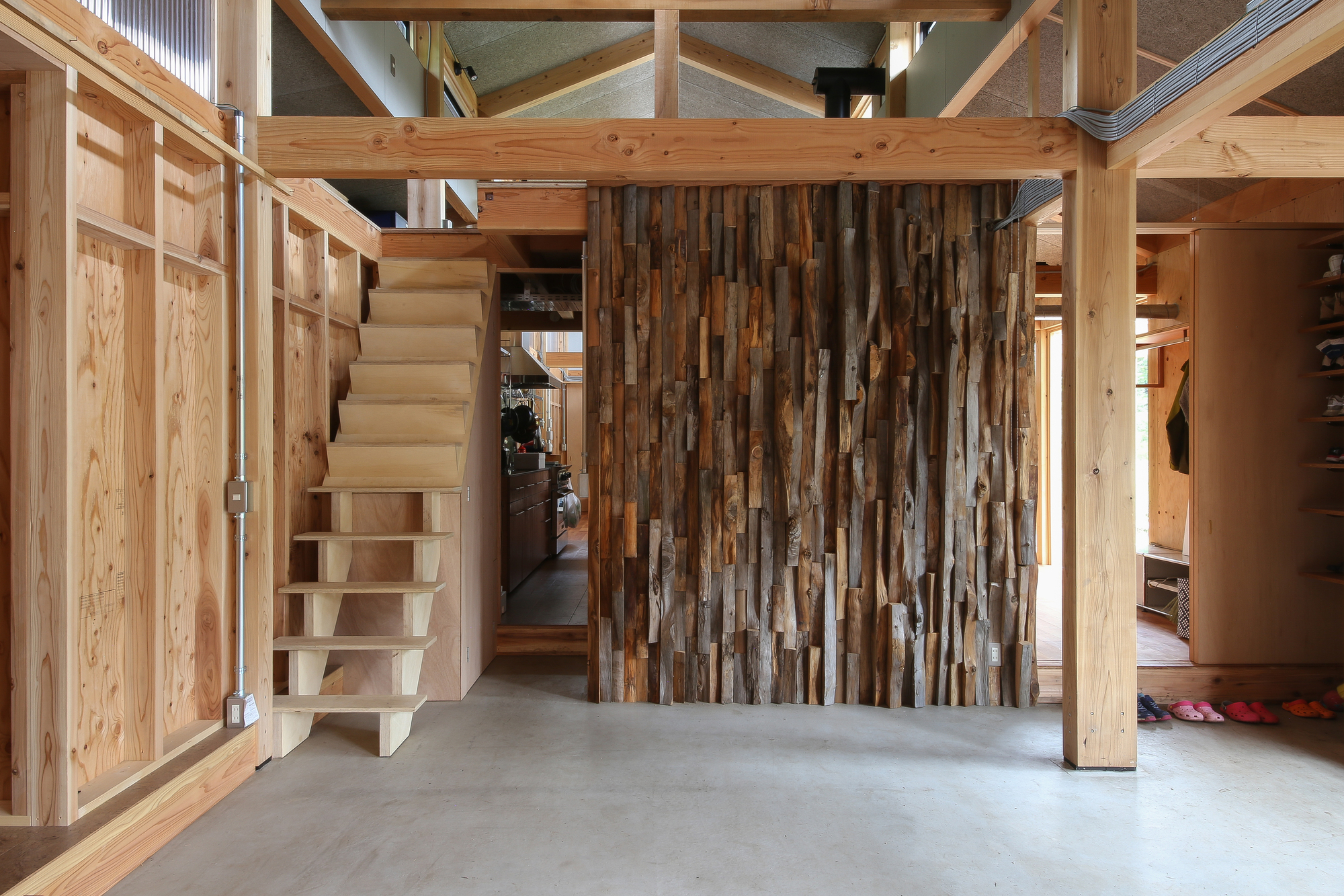 Entry hall with alternating timber board partition wall, floating plywood stair and polished concrete floor