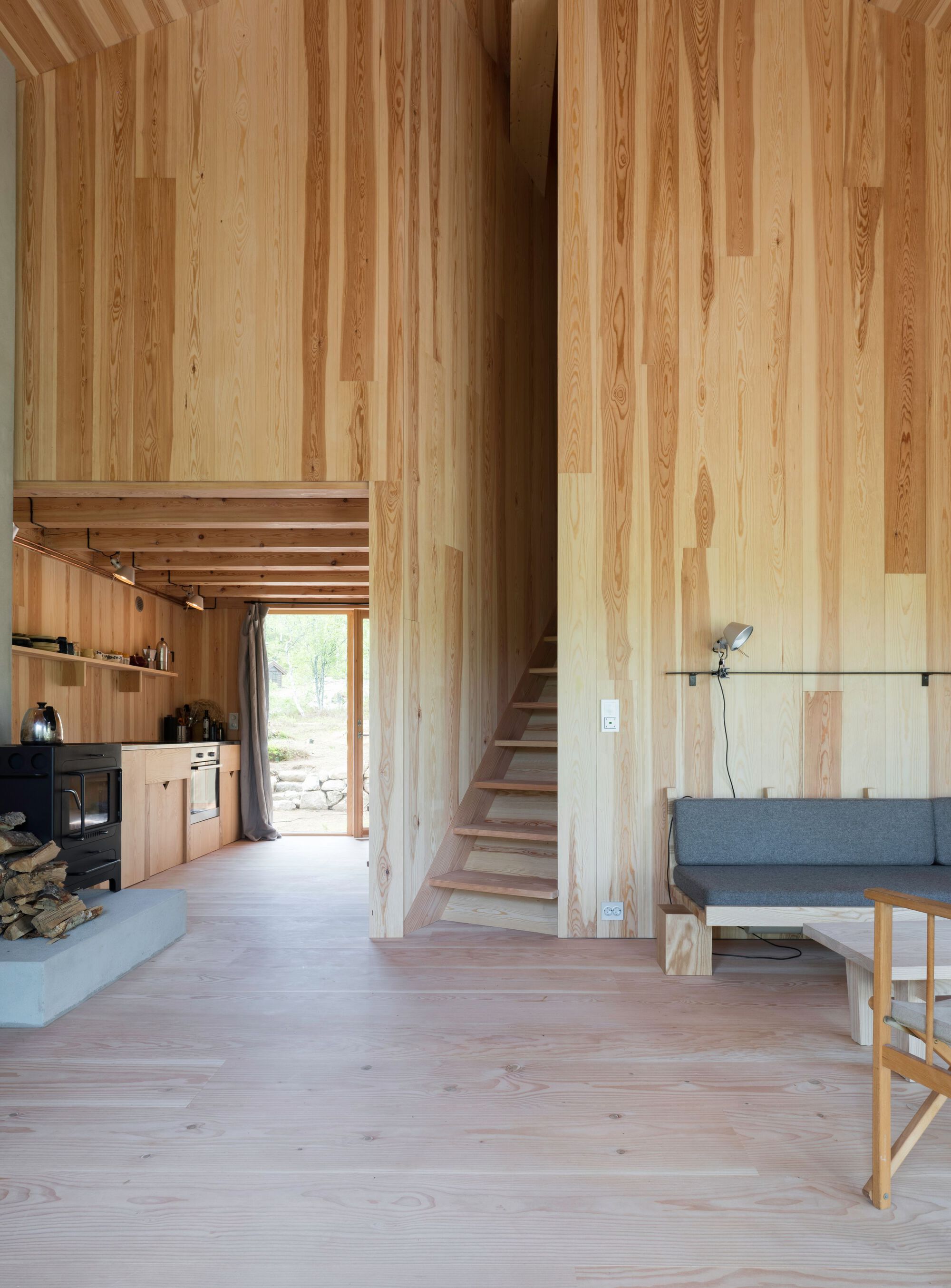 Double-height interior with vertical timber paneling, open kitchen, and staircase leading to upper level