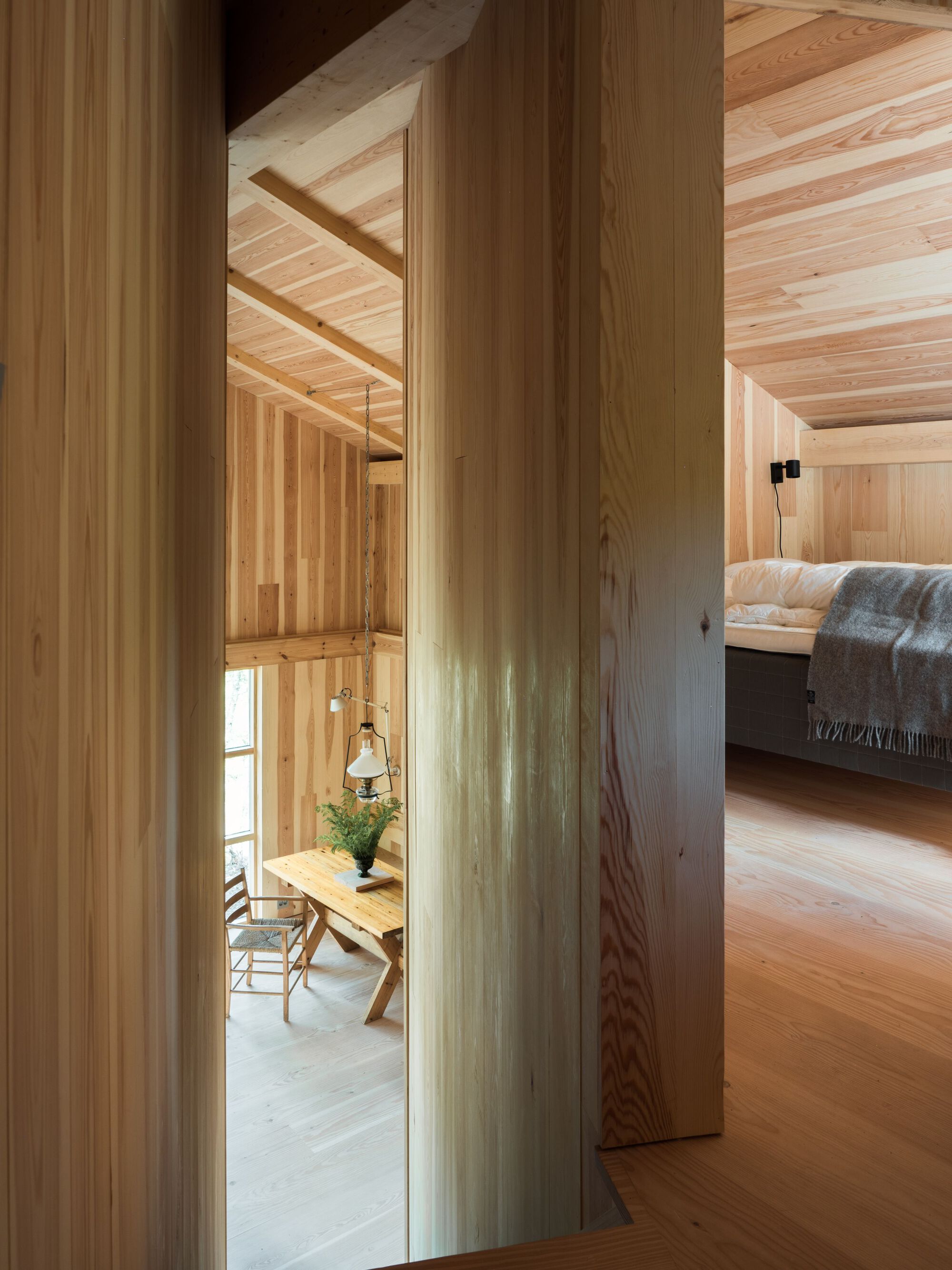 View through vertical wood columns toward dining area with hanging pendant and bedroom in background