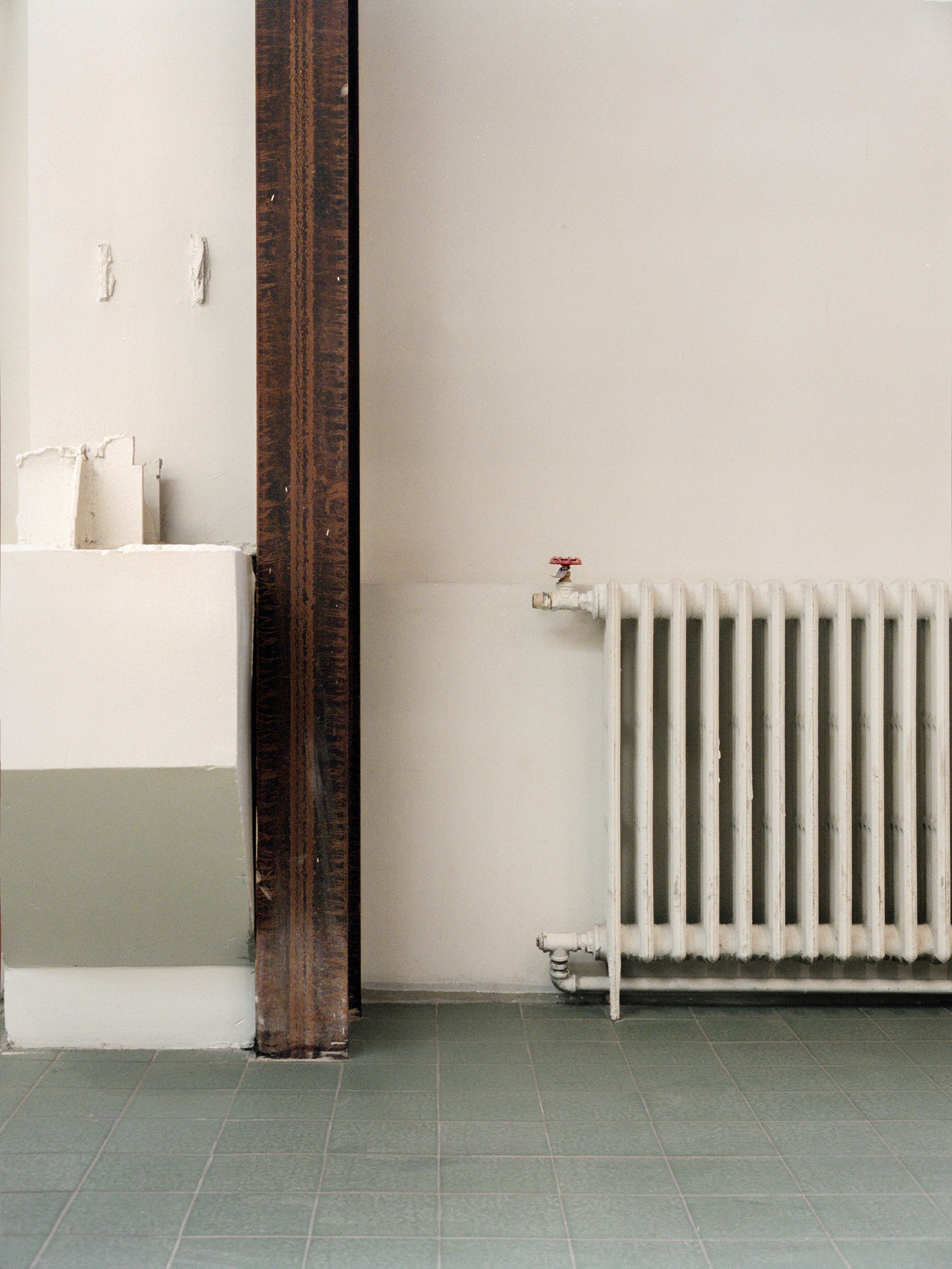 White radiator beside an exposed timber column and half-height partition on green tile flooring
