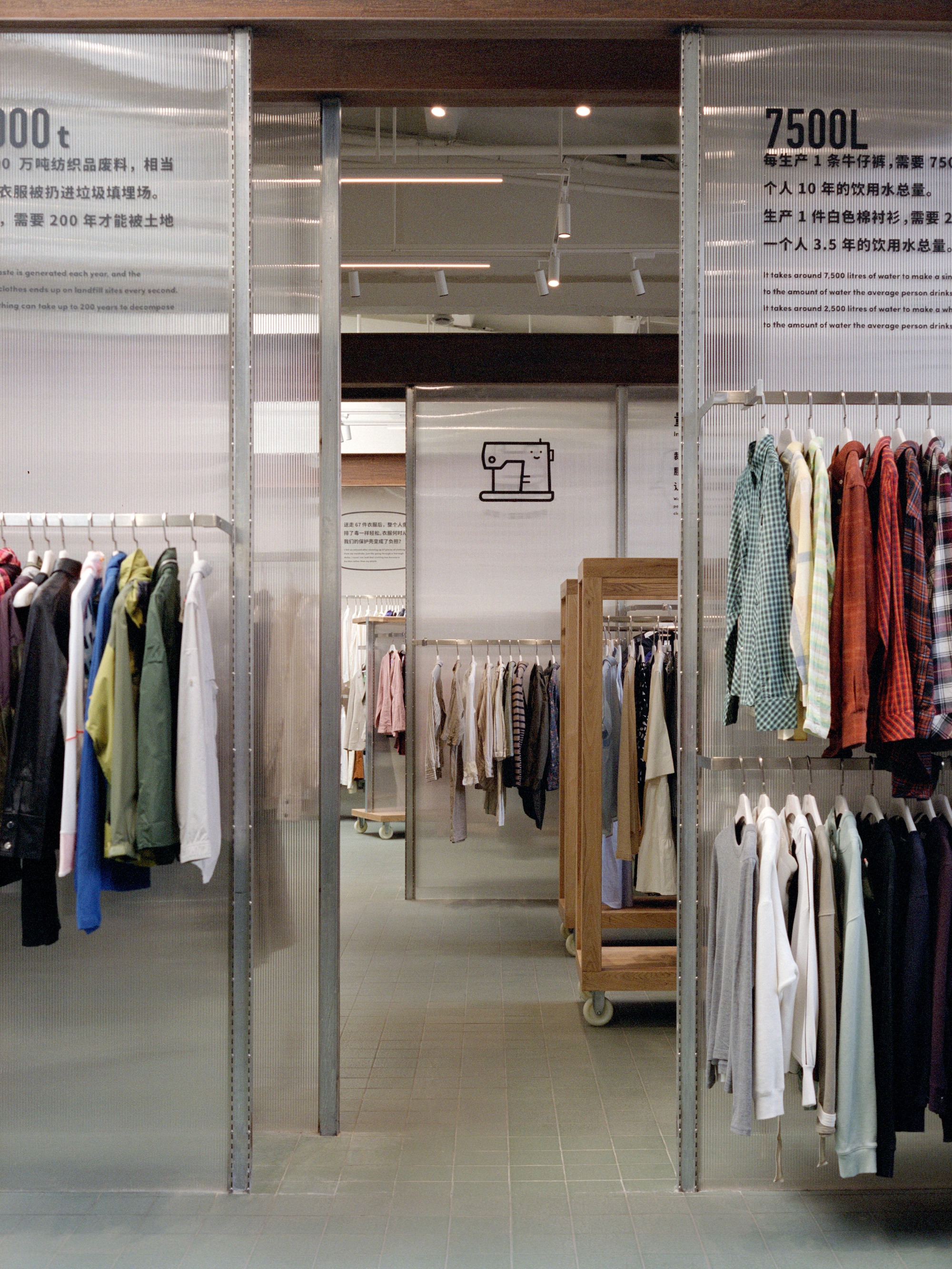 Clothing racks suspended from galvanized steel frames with translucent panels and graphic signage above
