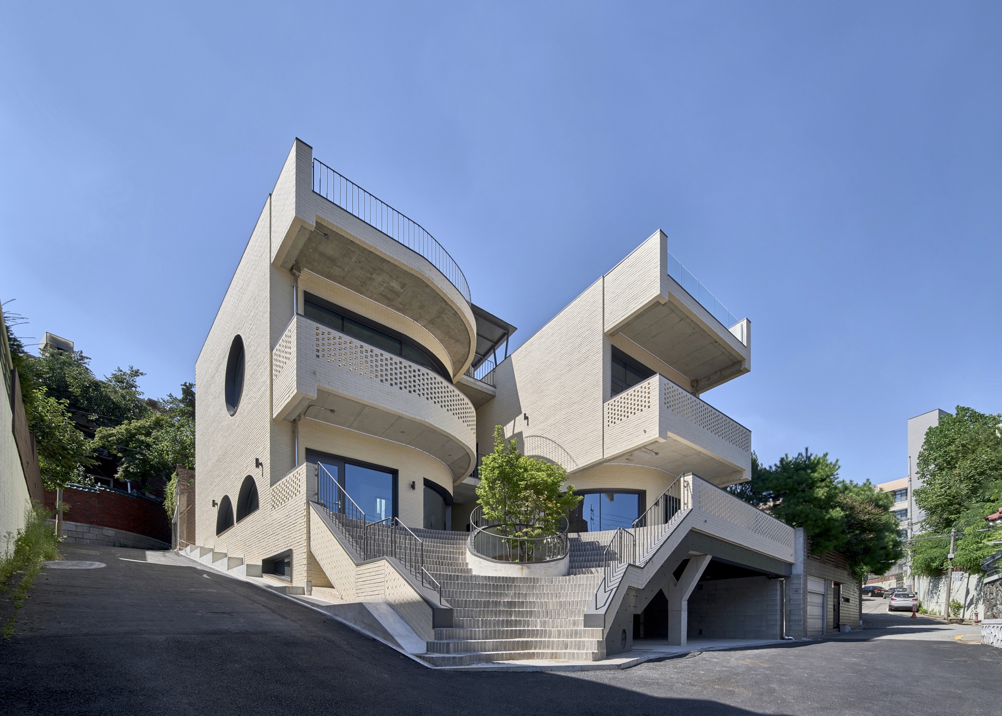 Street view of the stacked volumes with curved balconies and perforated brick screens under a clear sky
