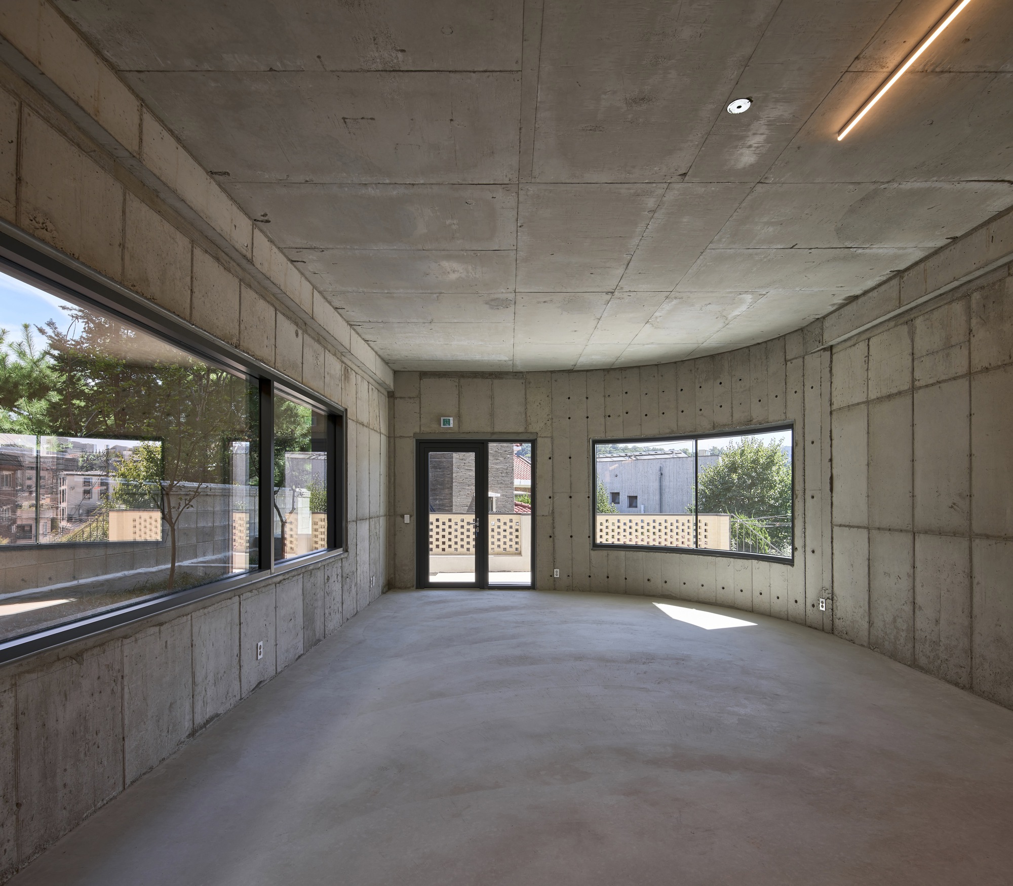 Interior room with board-formed concrete walls and ceiling illuminated by recessed linear lighting