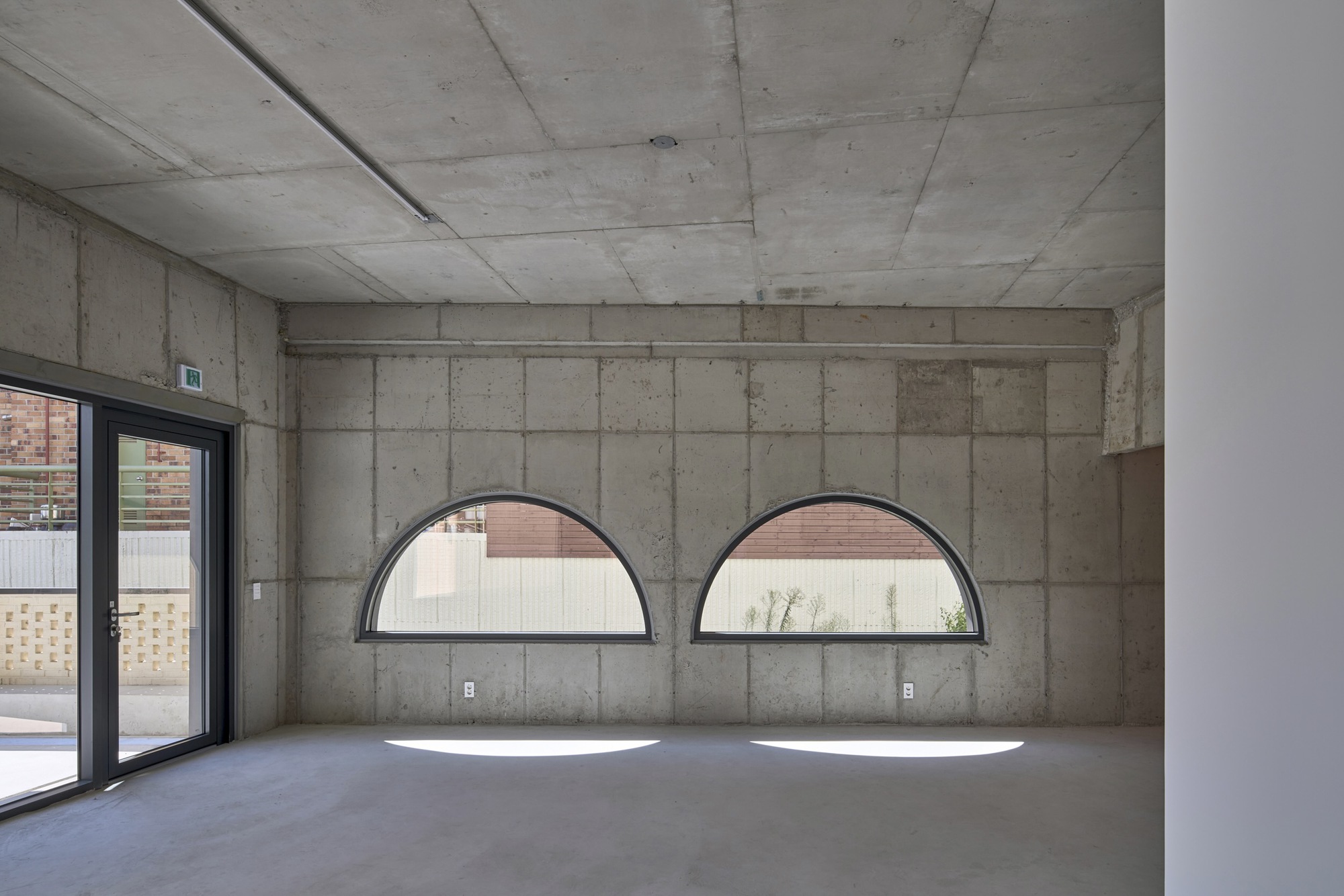 Exposed concrete interior wall with two semicircular windows casting shadows on the polished floor