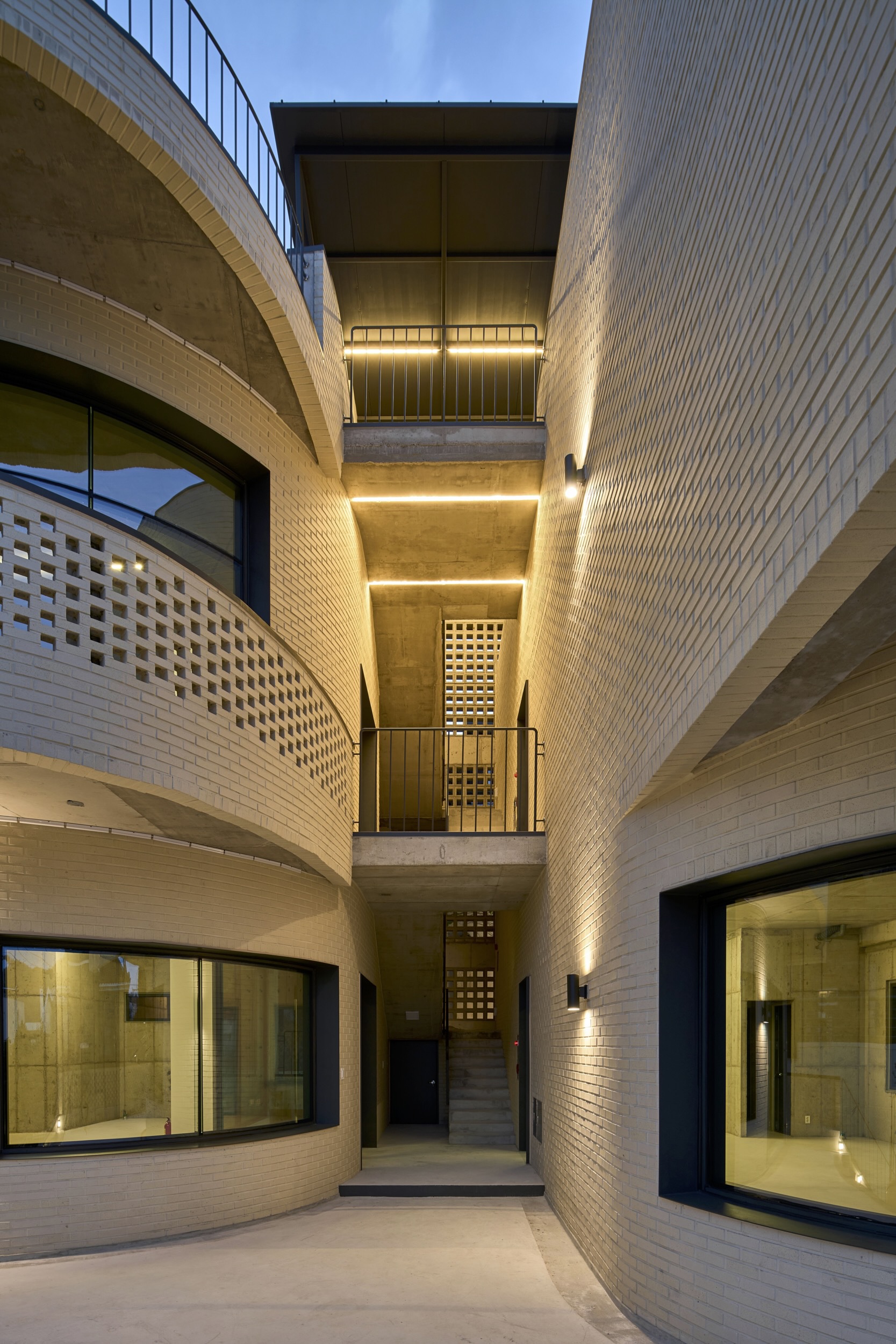 Vertical light well in white brick with stacked balconies and perforated brick screens at dusk