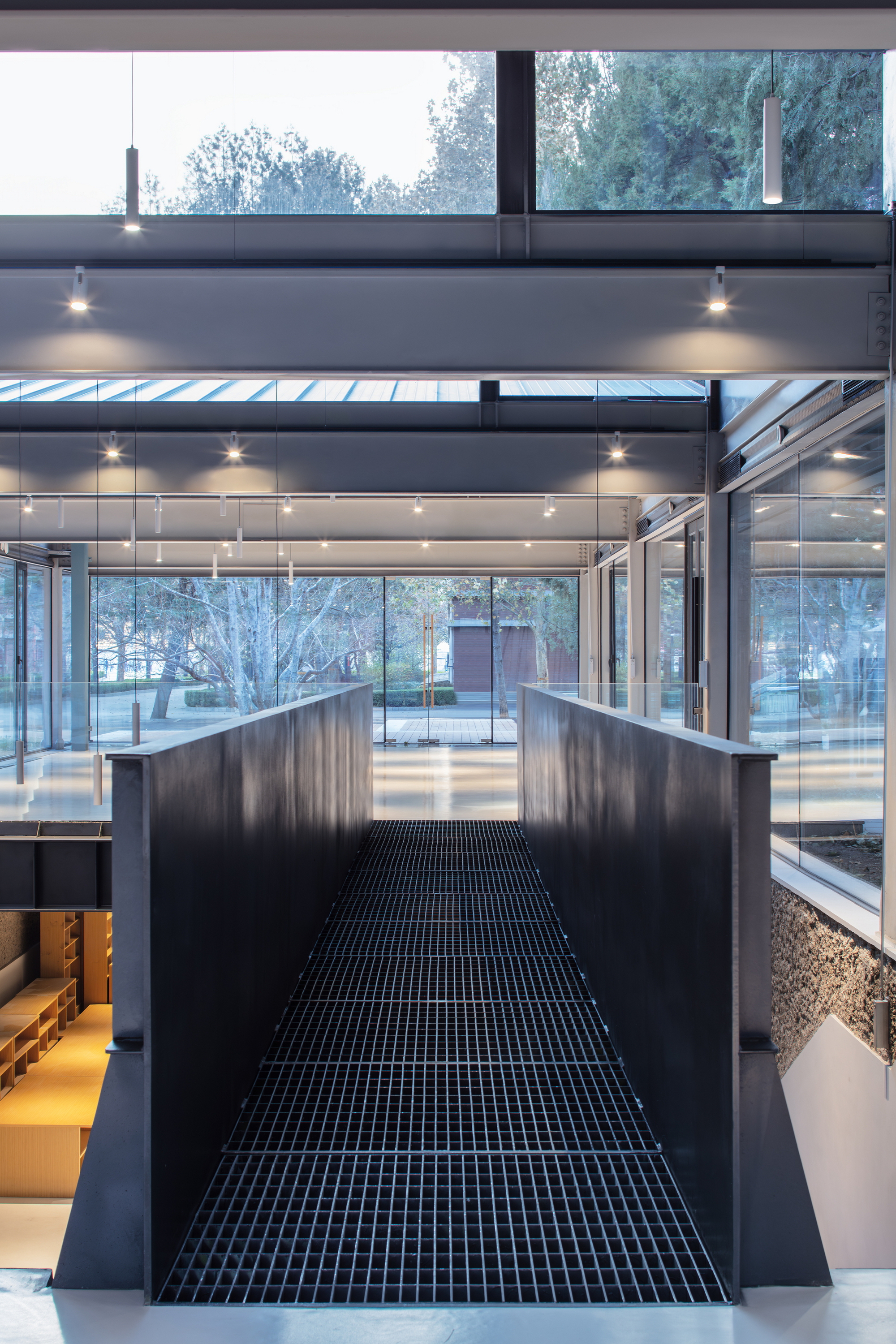 Central black grated bridge spanning between levels with full-height glazing overlooking exterior courtyard