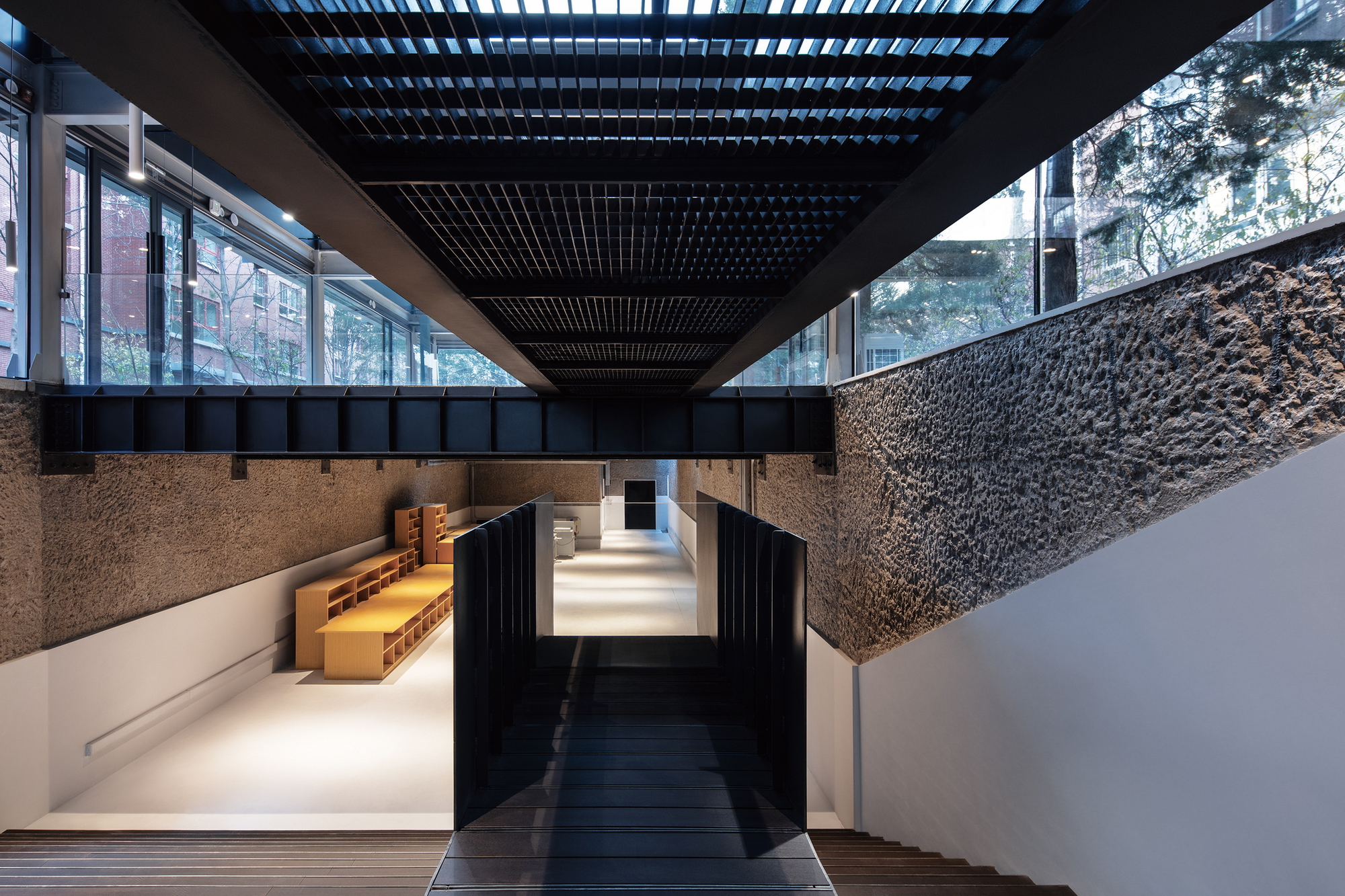 Interior passage showing textured stone walls, black timber overhead beams, and clerestory windows framing adjacent buildings