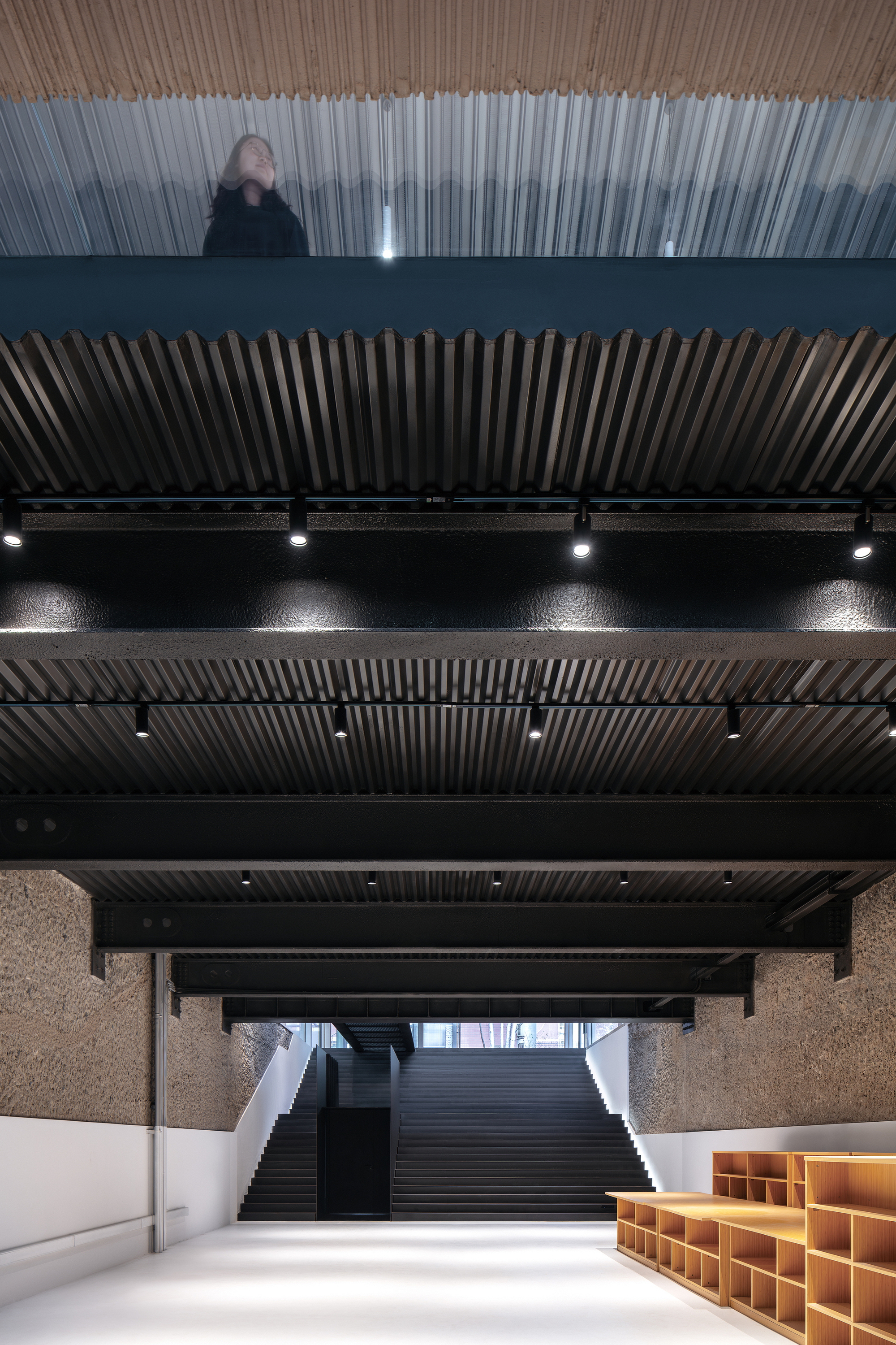 Upward view of stacked floor levels with vertical slat screens and a visitor standing on the translucent balcony