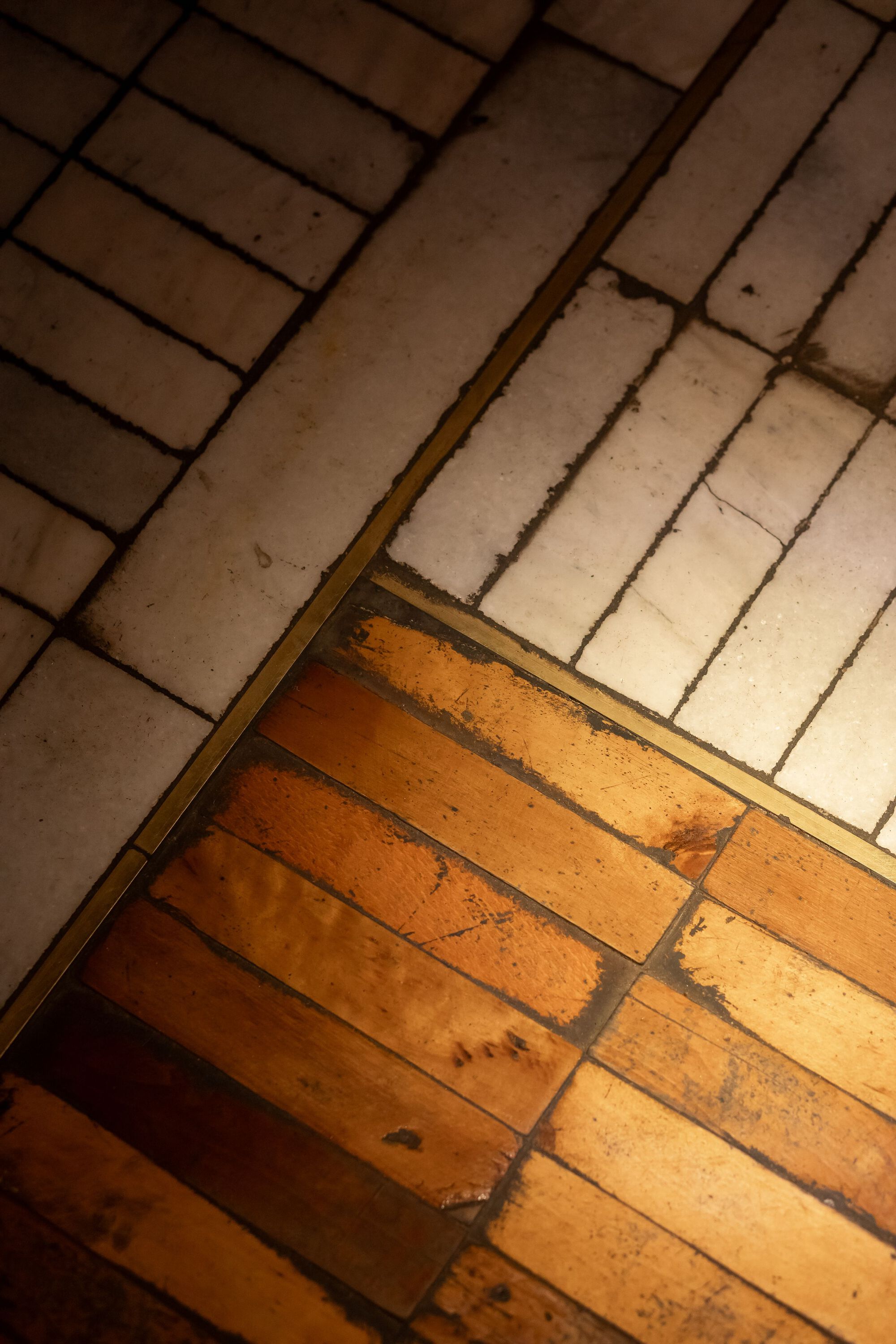 Diagonal threshold where weathered timber floorboards meet white ceramic tiles at differing orientations